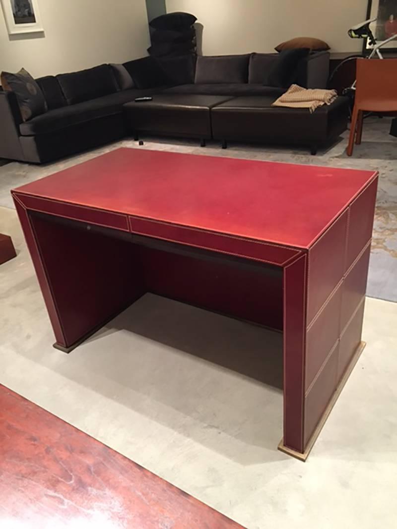 This elegant handmade leather-upholstered desk by Promemoria features red-brown leather with contrast stitching all the way around, a bronze base and two drawers with wooden interiors. The desk is in good condition with no tears or holes, only some