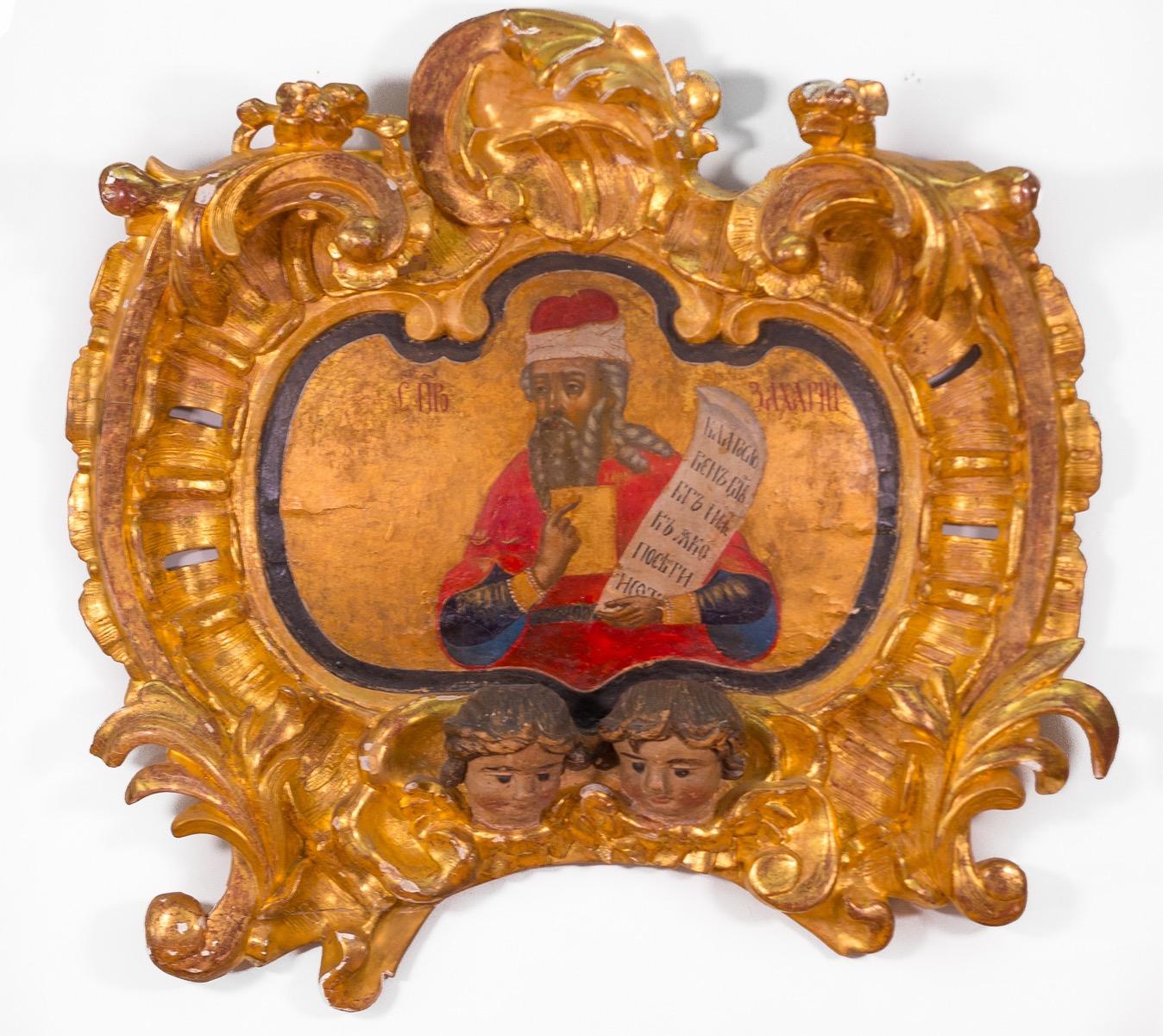 18th Century Russian Orthodox icon of the prophet Zachariah painted on an ornate solid slab of wood with an incorporated gold gilded frame that has been carved with a rococo design of deep scrolls and high relief. Incorporating at the base are two