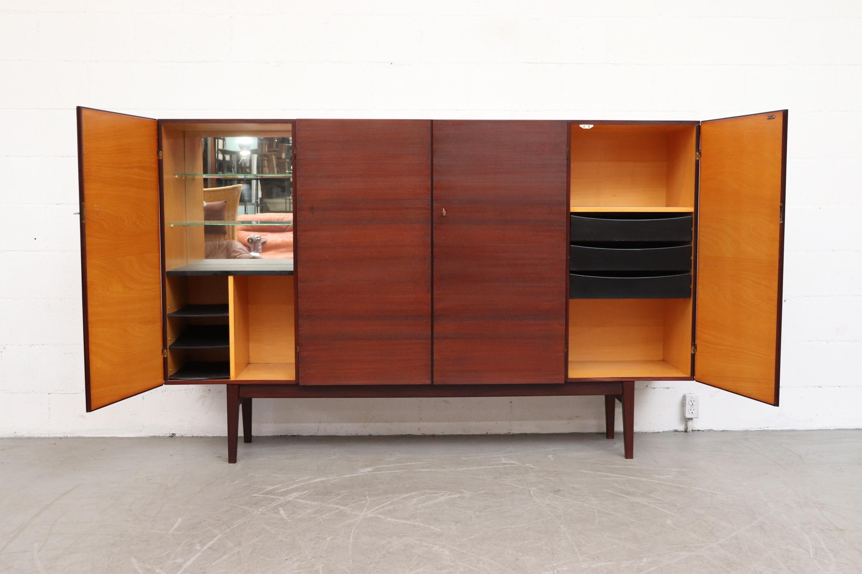 Mid century, large and tall dark teak sideboard with attractively contrasting blonde Interior by Hulmefa in the 1960's. Doors open to reveal shelves and small wet bar with mirrored back. lightly refinished wood, The piece is in otherwise good