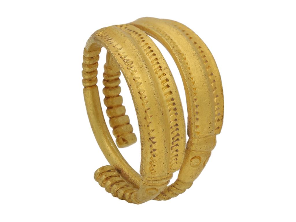 Proto-Viking gold zoomorphic ring. A yellow gold sinuous penannular ring, composed of two ridged plaques (or bodies) with incised decoration, each flanked to both sides by a pair of eyes and terminating in a ribbed shank, all smoothly spiralling