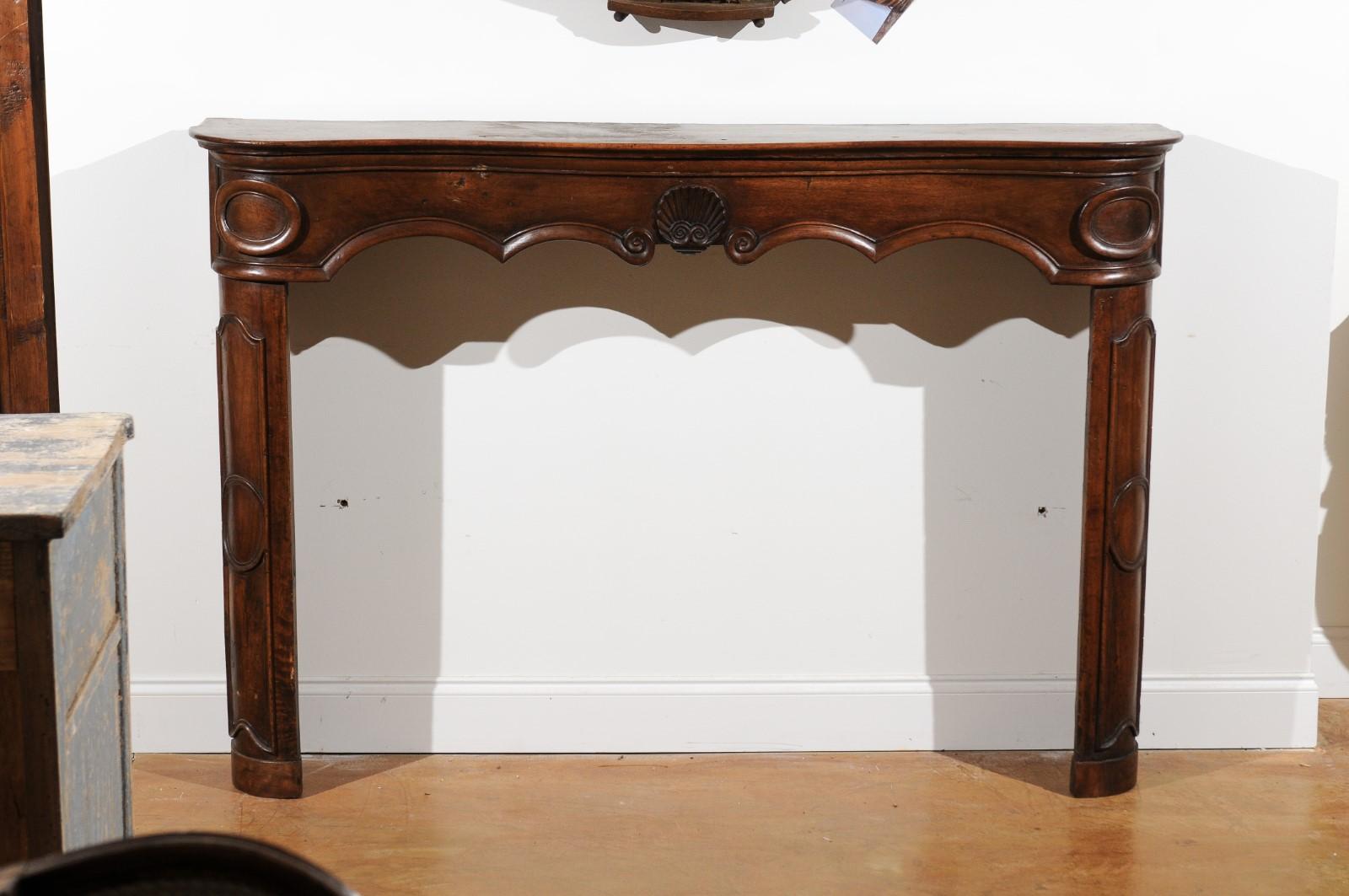 A French Louis XV period Provençal walnut fireplace mantel from the 18th century, with carved shell. Born in Provence during the 18th century, this walnut fireplace mantel features a serpentine top sitting above a lovely scalloped apron adorned with