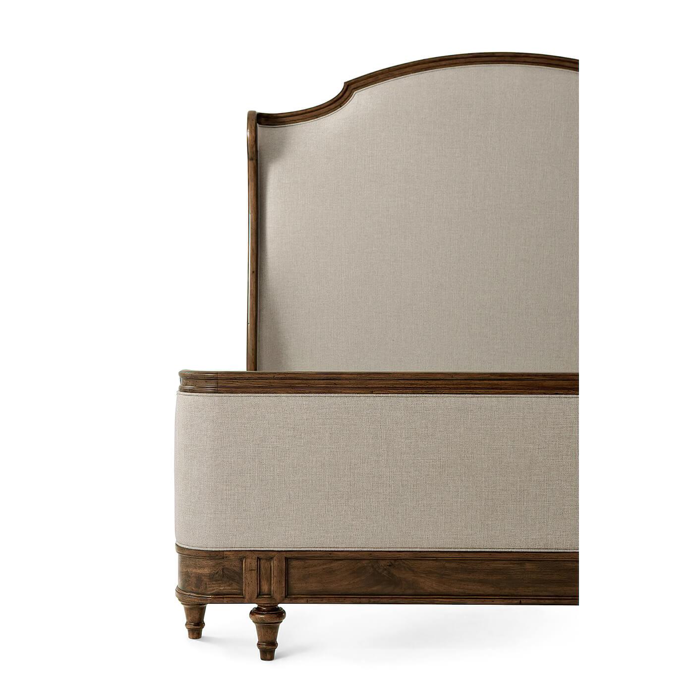 A French Provincial carved California King size bed with an arched and molded upholstered headboard with scroll wings, an upholstered and hand-carved framed low footboard, and paneled rails on turned and tapered toupee feet. 
Dimensions: 77.75