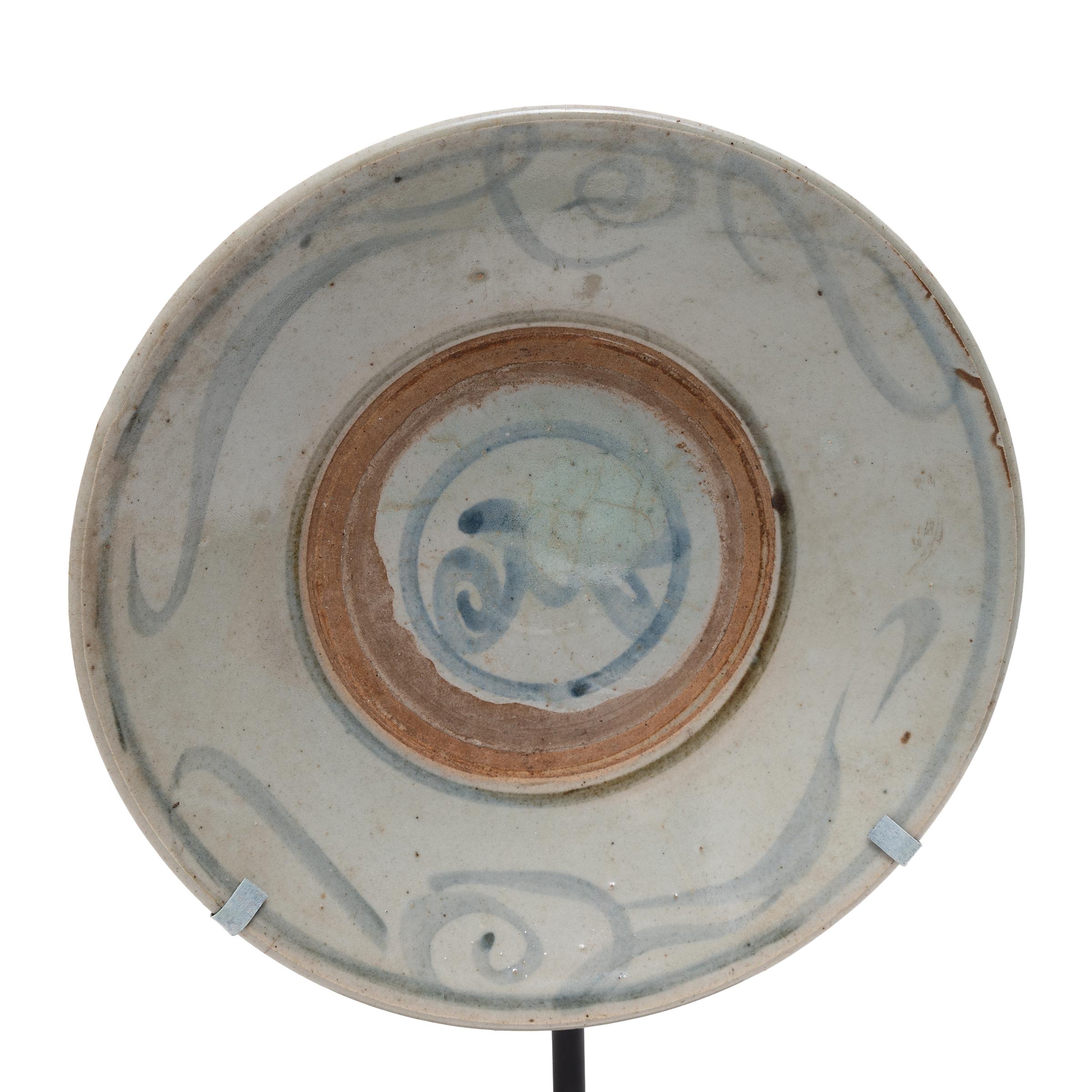 Calligraphic sweeps of blue bring this 19th-century footed plate to life, brushed atop a blue-grey glaze that cloaks its simple ceramic form. Once used as an everyday serving dish, this rustic plate has been reimagined as a tabletop sculpture,