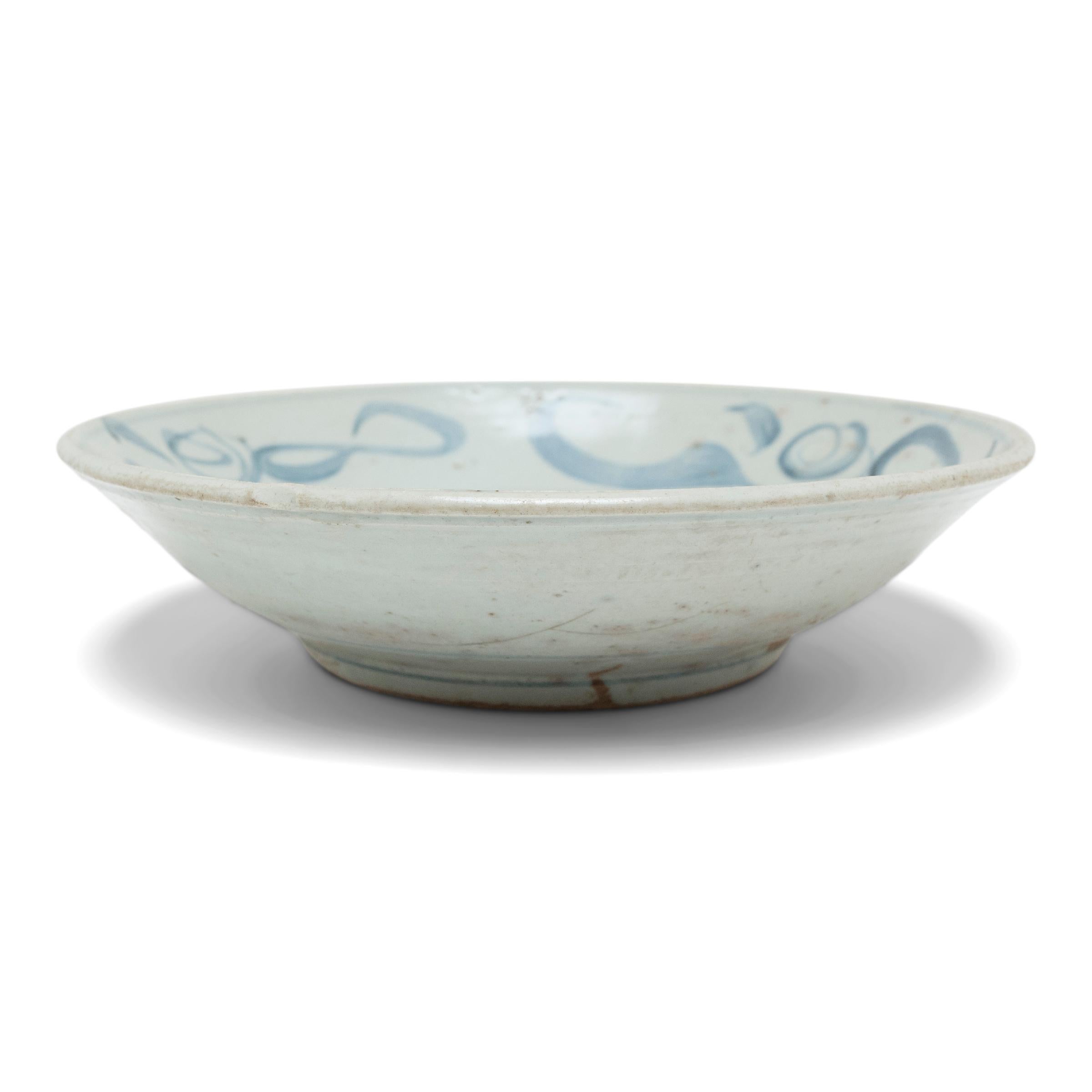 This mid-19th century footed plate is cloaked in a cool, off-white glaze and brushed with calligraphic sweeps of blue, bringing life and character to its simple ceramic form. Once used as an everyday serving dish, this expressive example of Chinese