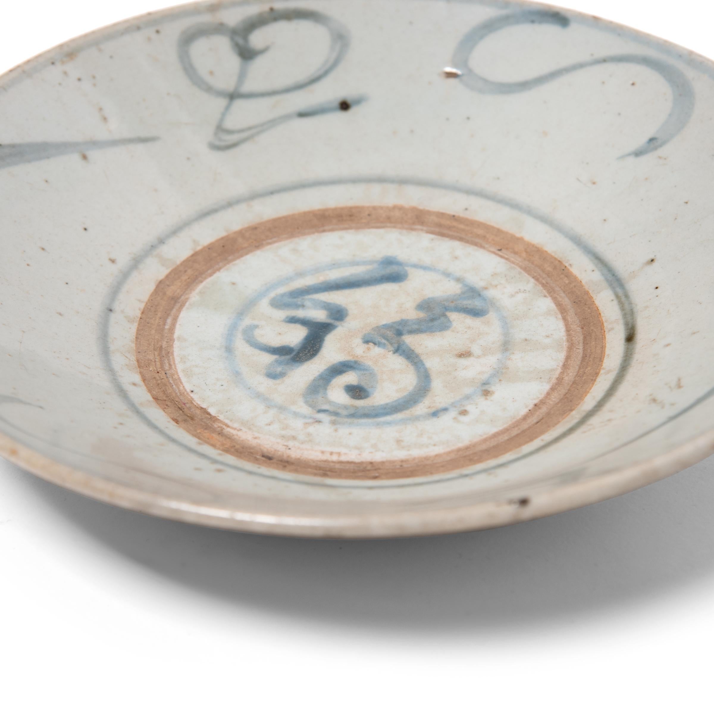 Calligraphic sweeps of blue bring this 19th century footed plate to life, brushed atop a blue-grey glaze that cloaks the simple ceramic form. Once used daily for tea, rice, and soup, this expressive example of Chinese blue and white ceramics can