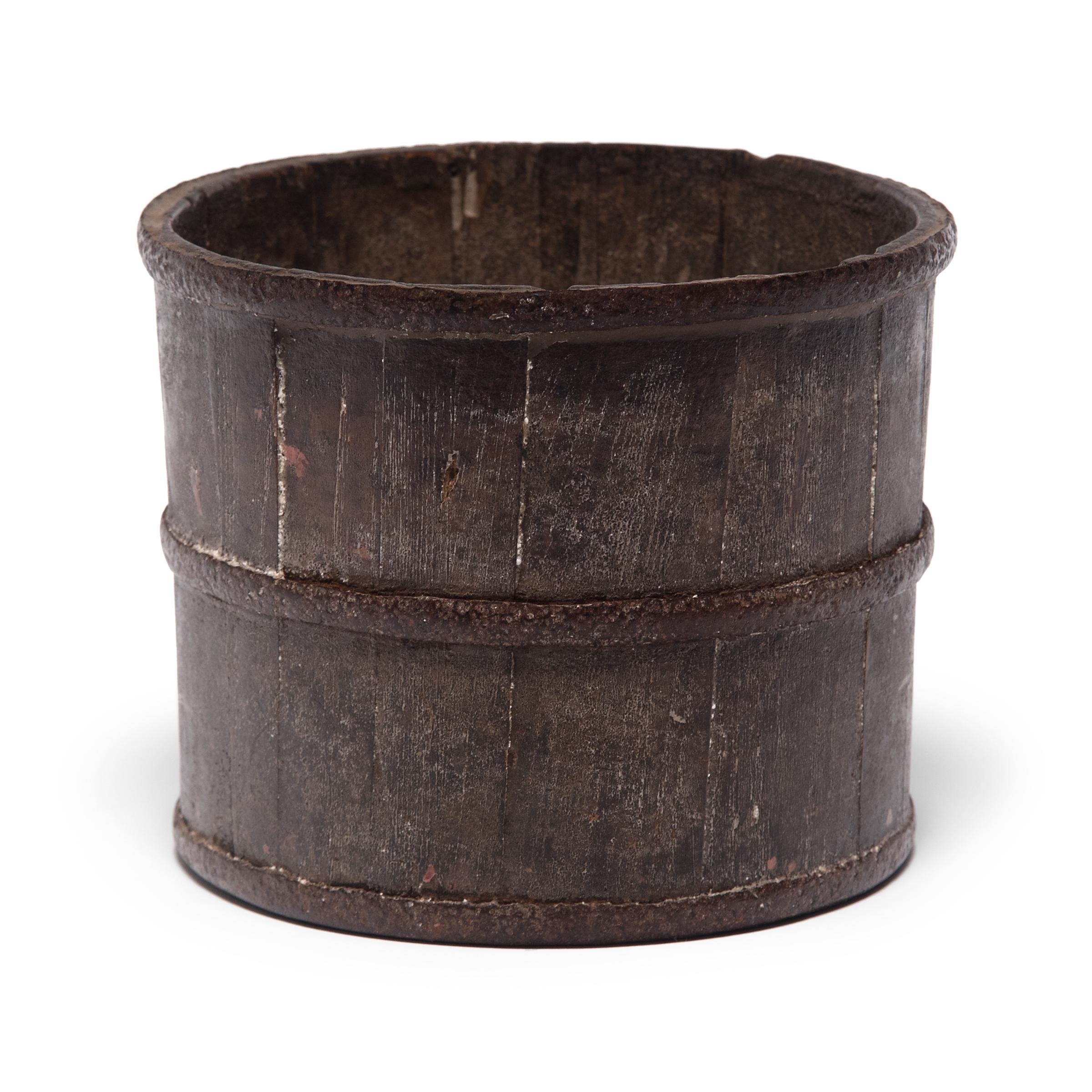 Placed beside his inkpot and insktone, this 19th century brush pot once held select calligraphy brushes in a scholar’s studio. Cloaked in a rich patina, the vessel is simply designed with finely joined pinewood slats held together by hand-smithed