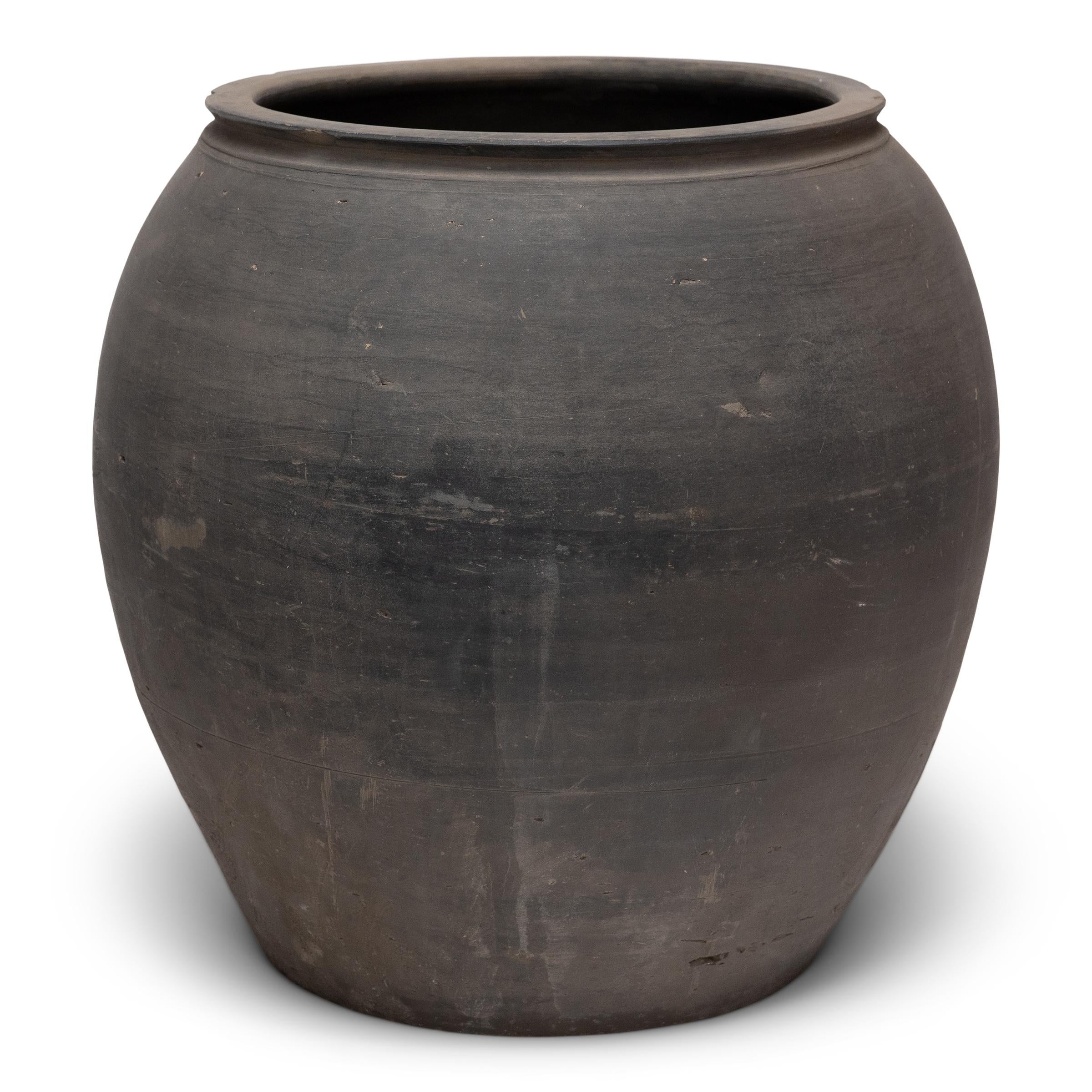 Scolpito all'inizio del XX secolo nella provincia cinese dello Shanxi, questo vaso di argilla ha un esterno grigio fumo con proporzioni equilibrate e una superficie non smaltata splendidamente irregolare. Incaricato dell'umile compito di conservare