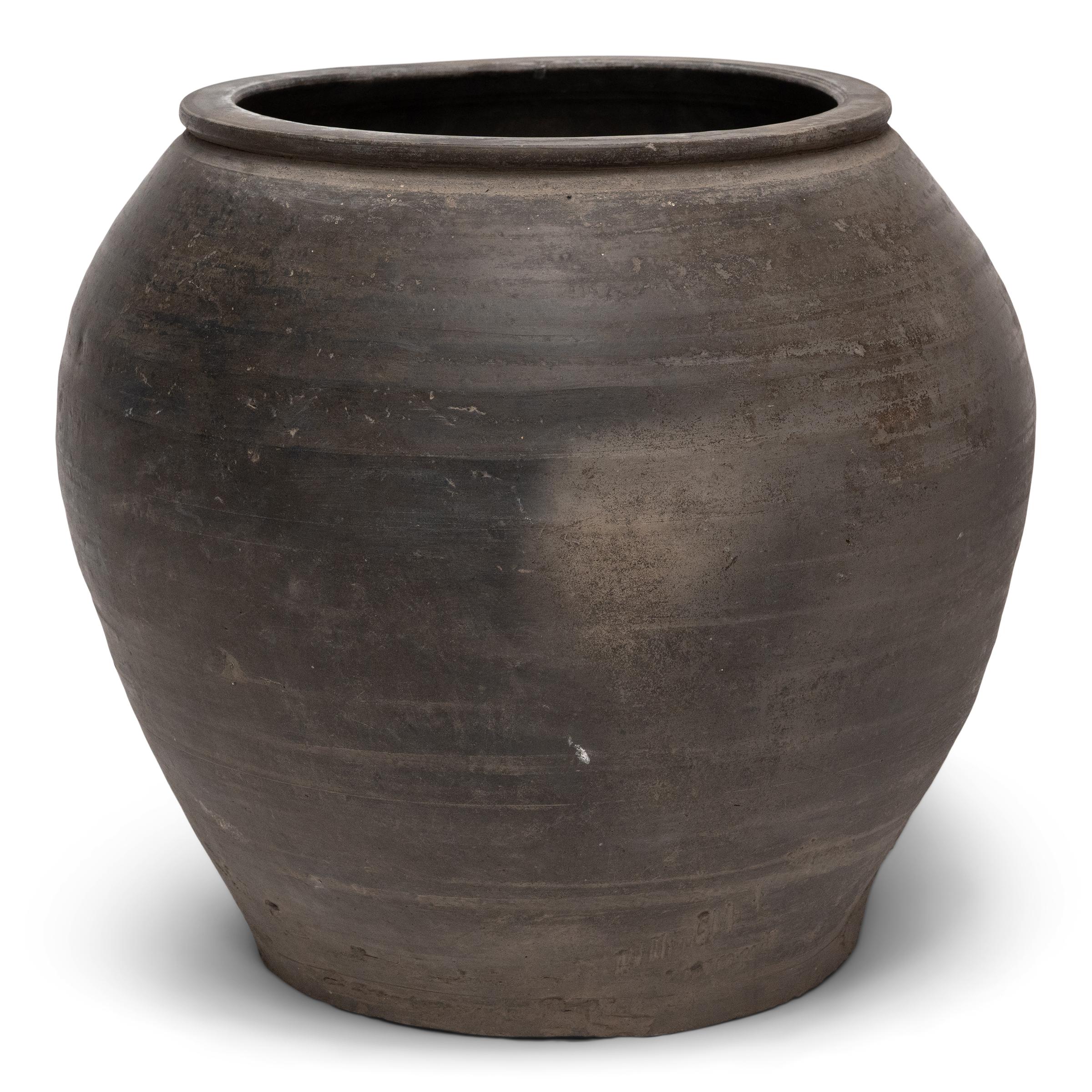 Sculpted during the early 20th century in China's Shanxi province, this clay vessel has a smoky grey exterior with balanced proportions and a beautifully irregular unglazed surface. Charged with the humble task of storing dry goods, the jar has a