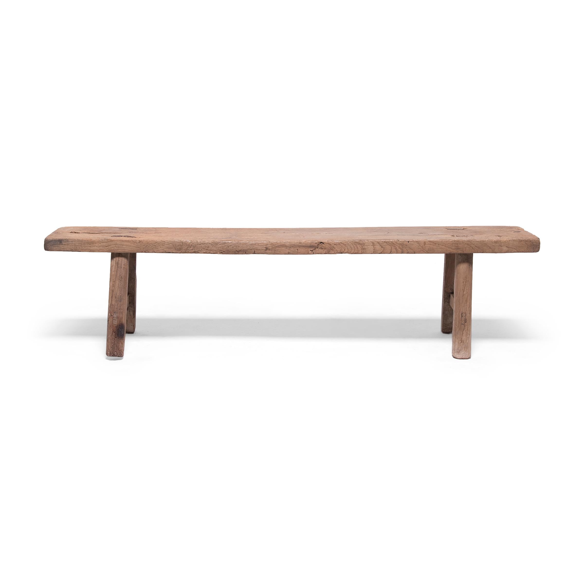 Embracing the raw beauty of unworked wood, this low bench from Hebei province is made from a single piece of unfinished elmwood timber. Dated to the late 19th century, the plank-top bench was crafted using mortise-and-tenon joinery techniques and