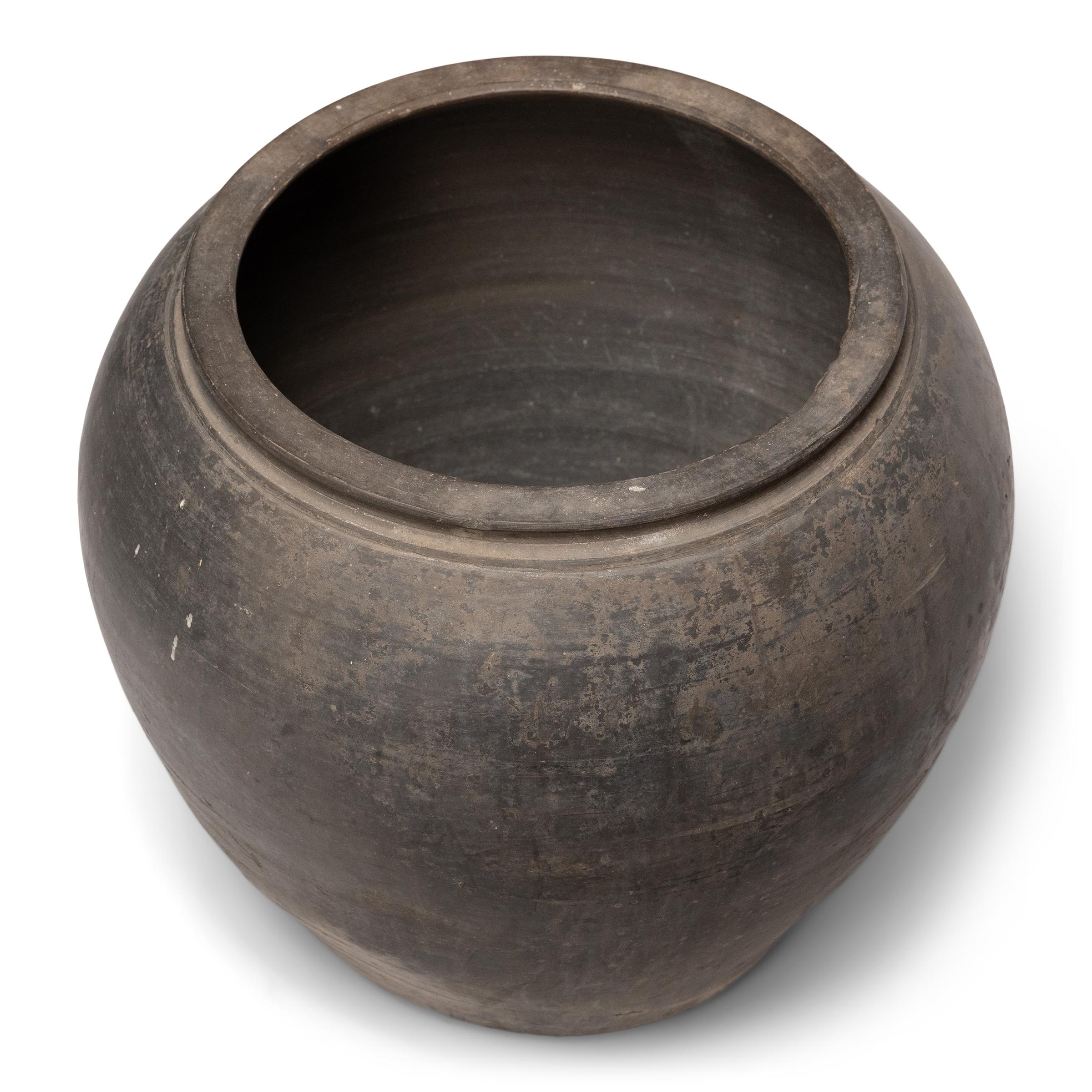 Sculpted during the early 20th century in China's Shanxi province, this terra cotta vessel has a smoky taupe exterior with balanced proportions and a beautifully irregular unglazed surface. Charged with the humble task of storing dry goods, this