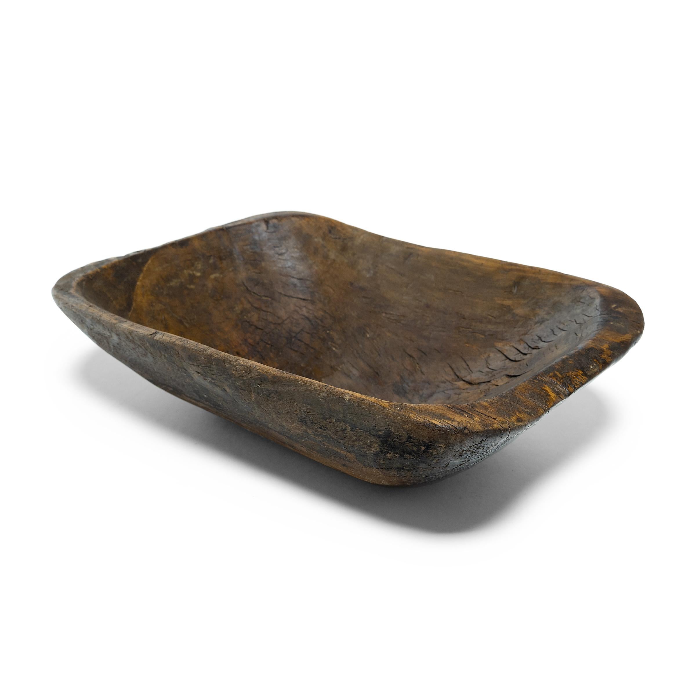 This wooden farm tray from northern China charms with its rustic finish and asymmetrical form. Hand-carved from a single block of wood, the large tray is truly one-of-a-kind, shaped with curved edges, tapered sides, and a deep interior basin. Years