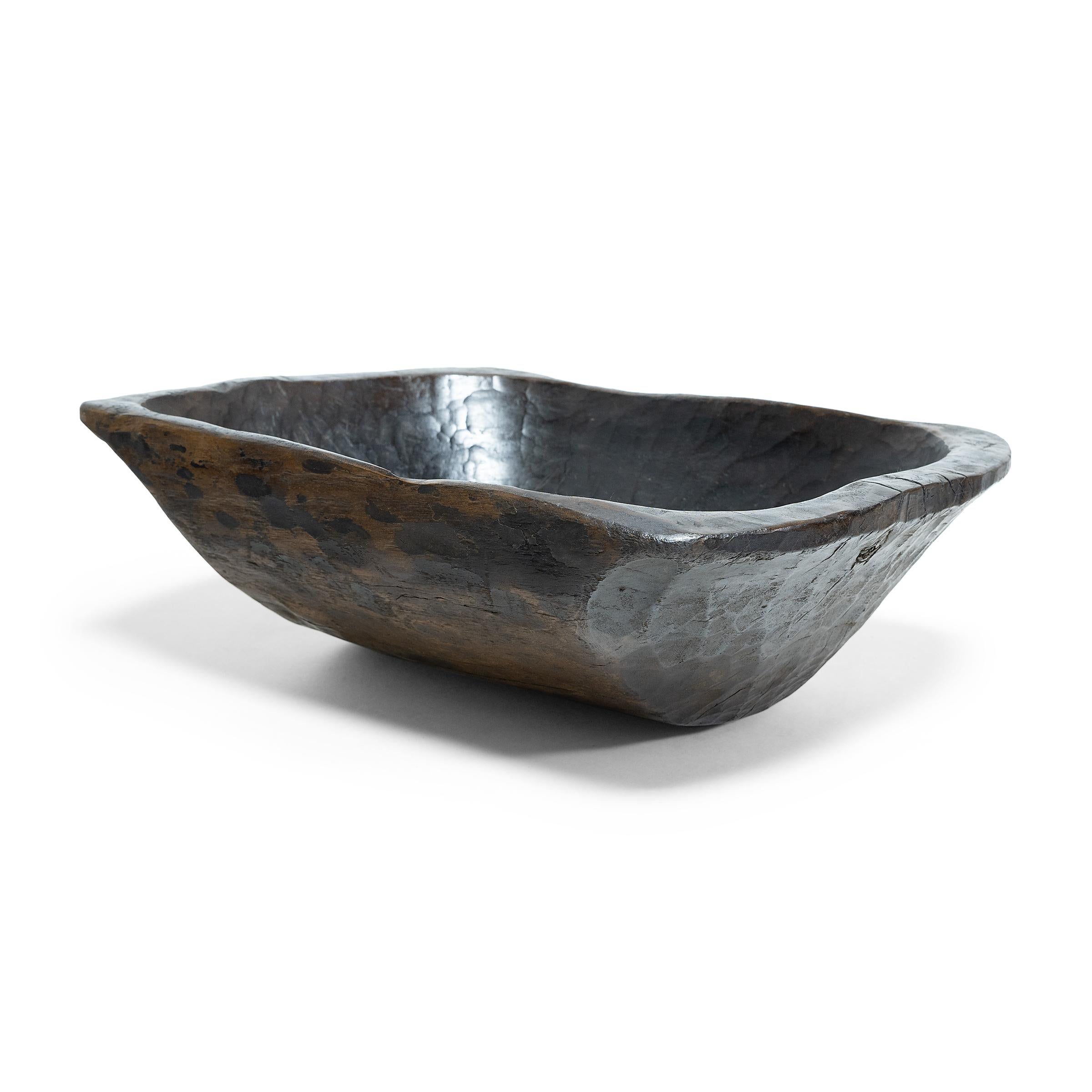 This wooden farm tray from northern China charms with its rustic finish and asymmetrical form. Hand-carved from a single block of wood, the large tray is truly one-of-a-kind, shaped with a deep basin and tapered sides that flatten at the rim. The