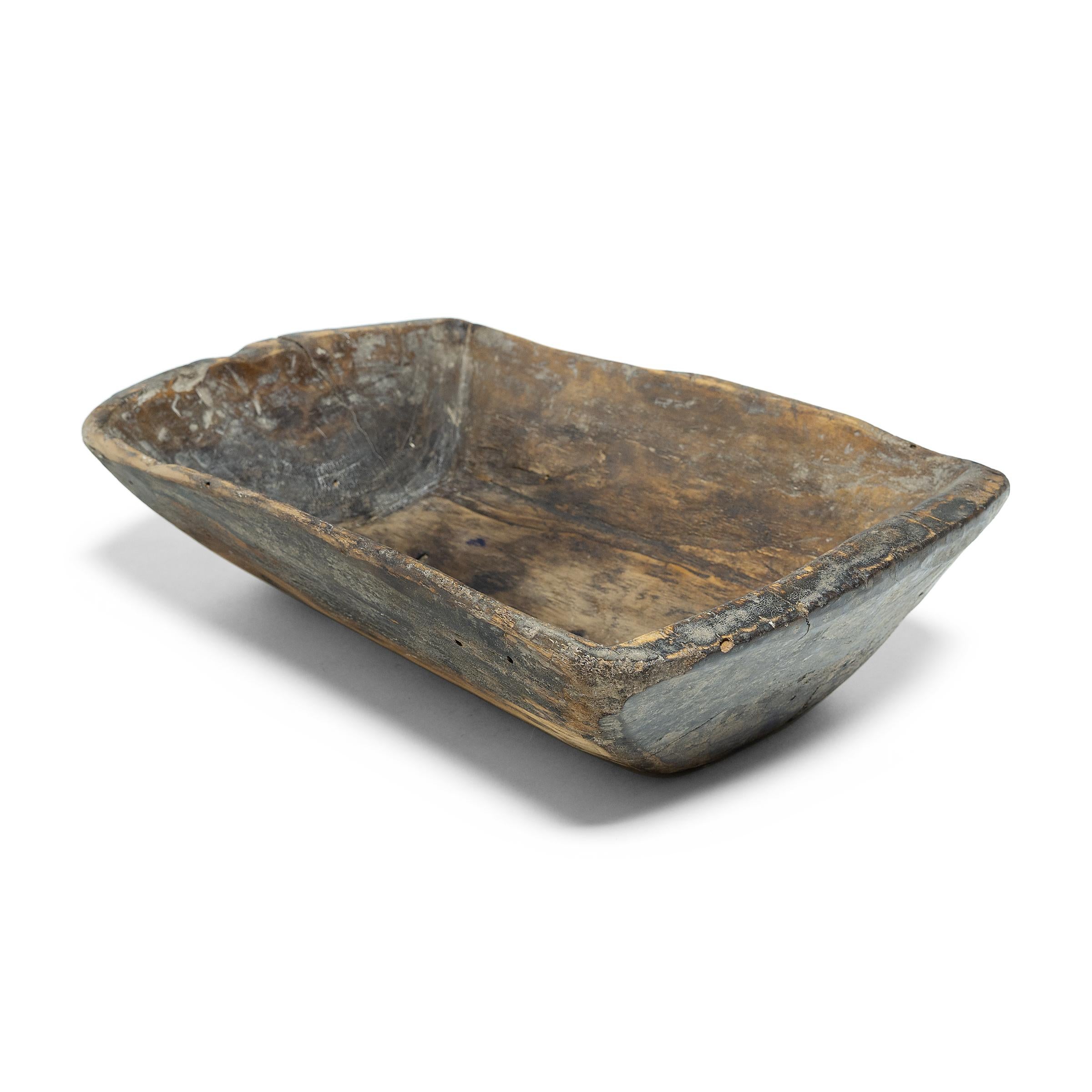 This wooden farm tray from northern China charms with its rustic finish and asymmetrical form. Hand-carved from a single block of wood, the large tray is truly one-of-a-kind, shaped with curved edges, tapered sides, and a deep interior basin. Years