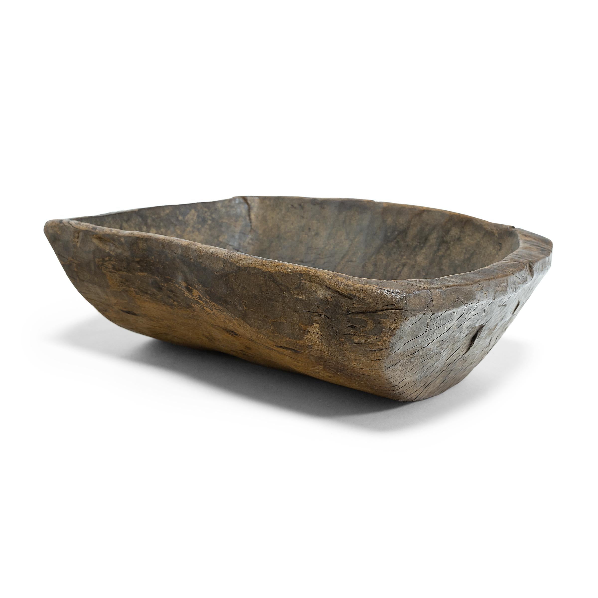This early-20th century wooden tray from northern China charms with rustic texture and asymmetric form. hand carved from a single block of wood, the tray has a rectangular shape with rounded corners, curved out tapered sides, and a thin rim. Years