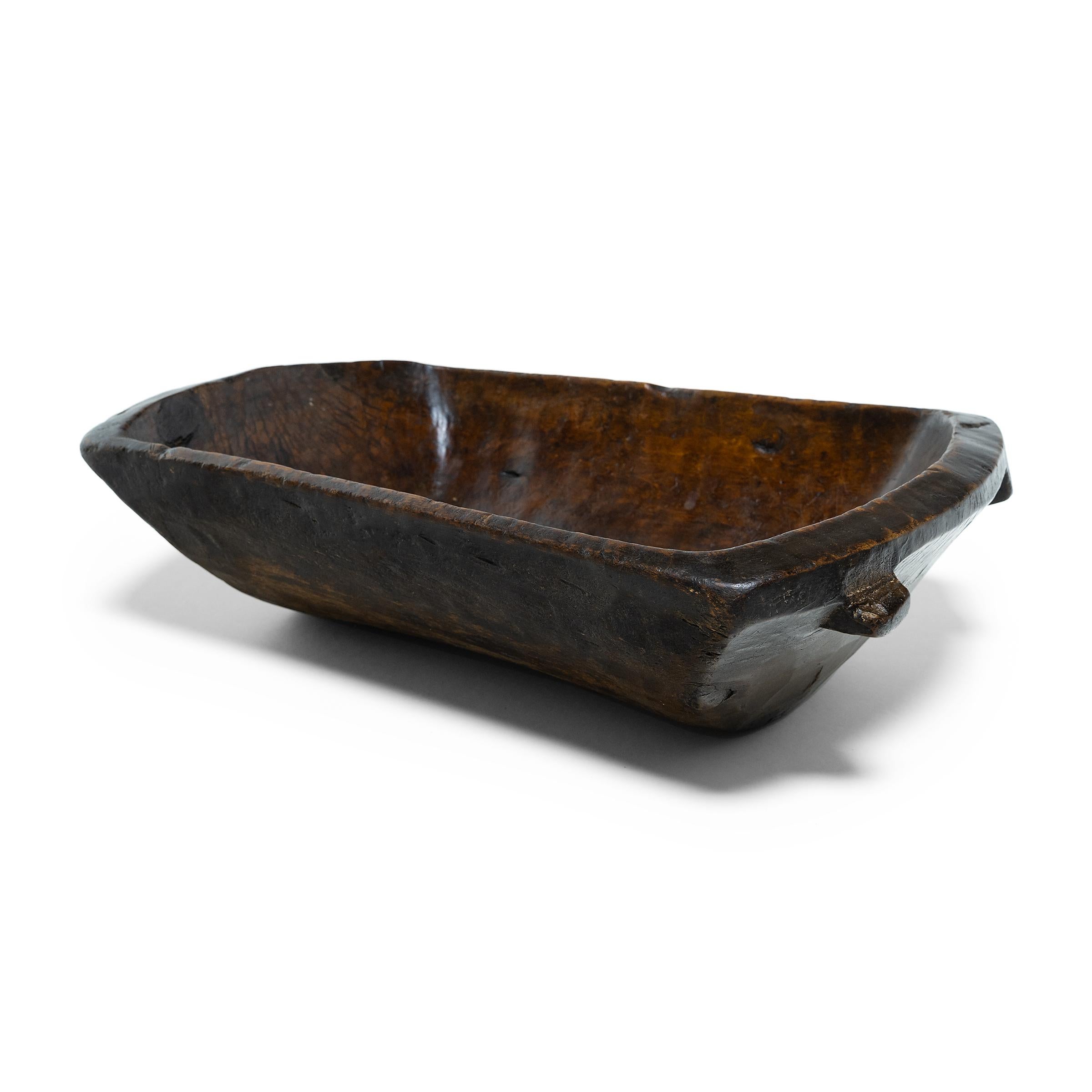 This early-20th century wooden tray from northern China charms with rustic texture and asymmetric form. Hand-carved from a single block of wood, the tray has a rectangular shape with rounded corners and tapered sides that flatten out at the rim.