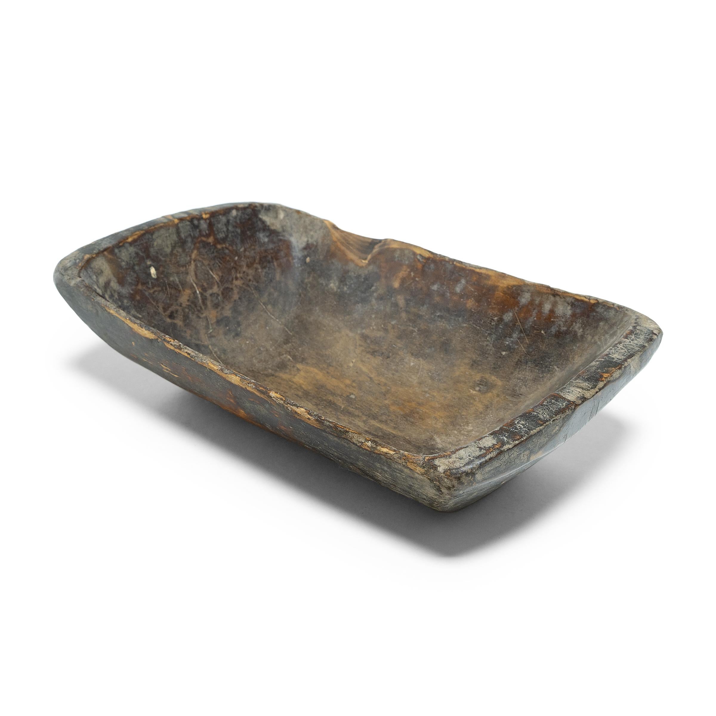 This wooden farm tray from northern China charms with its rustic finish and asymmetrical form. Hand-carved from a single block of wood, the tray is truly one-of-a-kind, shaped with a deep basin and tapered sides. The surface of the tray is faceted
