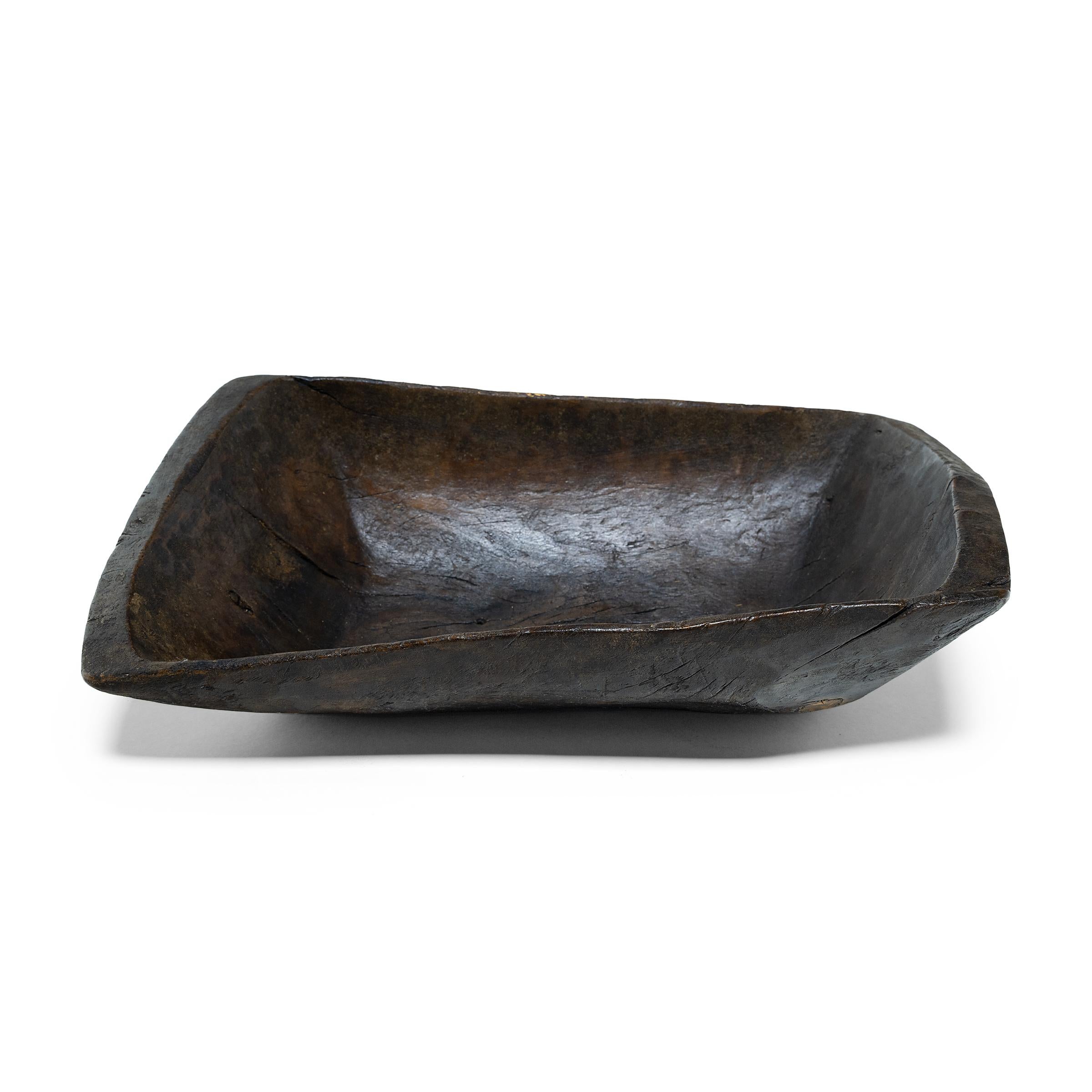 This early-20th century wooden tray from northern China charms with rustic texture and asymmetric form. Hand-carved from a single block of wood, the tray has a rectangular shape with rounded corners and tapered sides that flatten out at the rim.