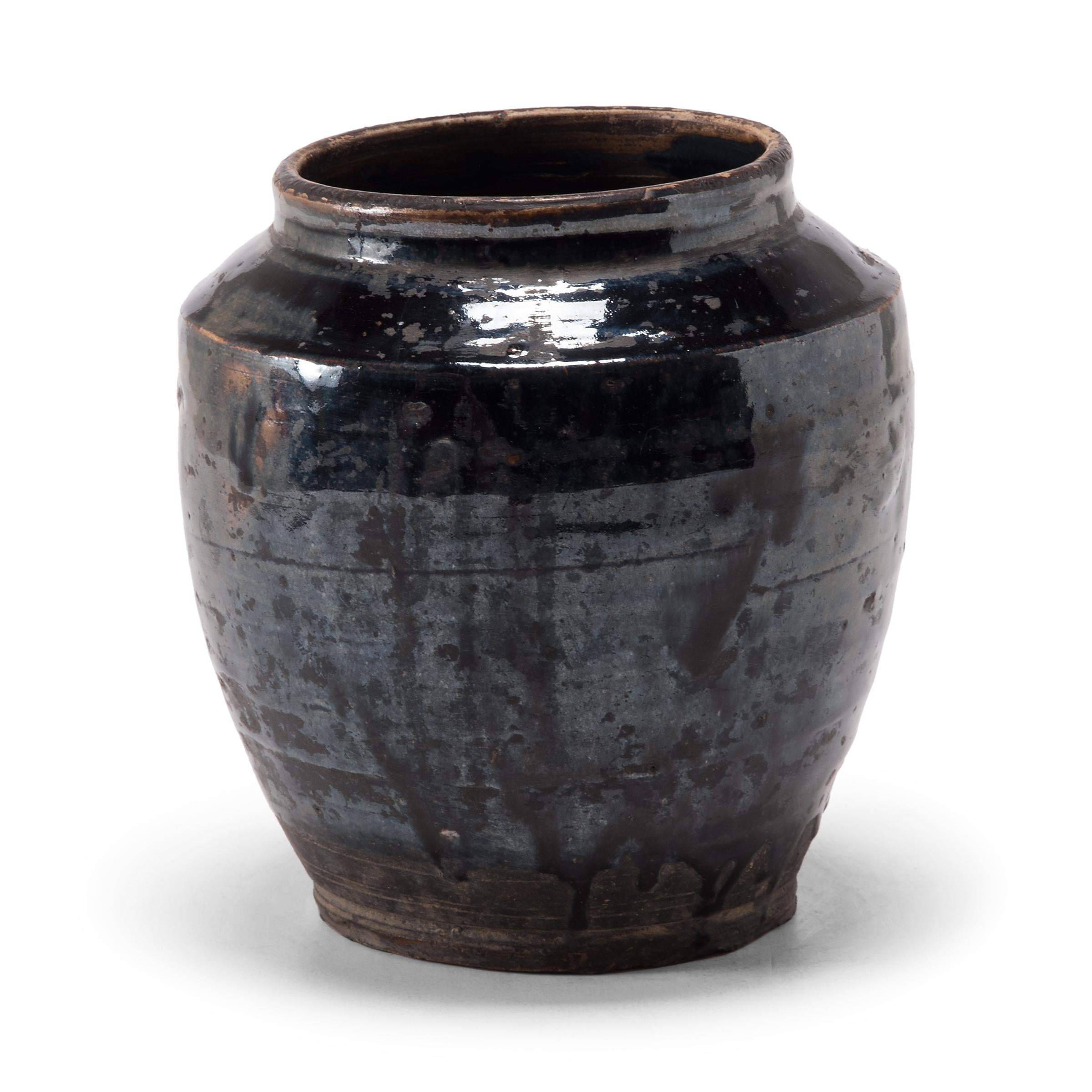 A dark glaze coats the angular body of this squat kitchen vessel, pooling in the shallow ridges along its sides with subtle iridescence. The petite early 20th century dish was once used for storing food in a Qing-dynasty kitchen, as evidenced by its