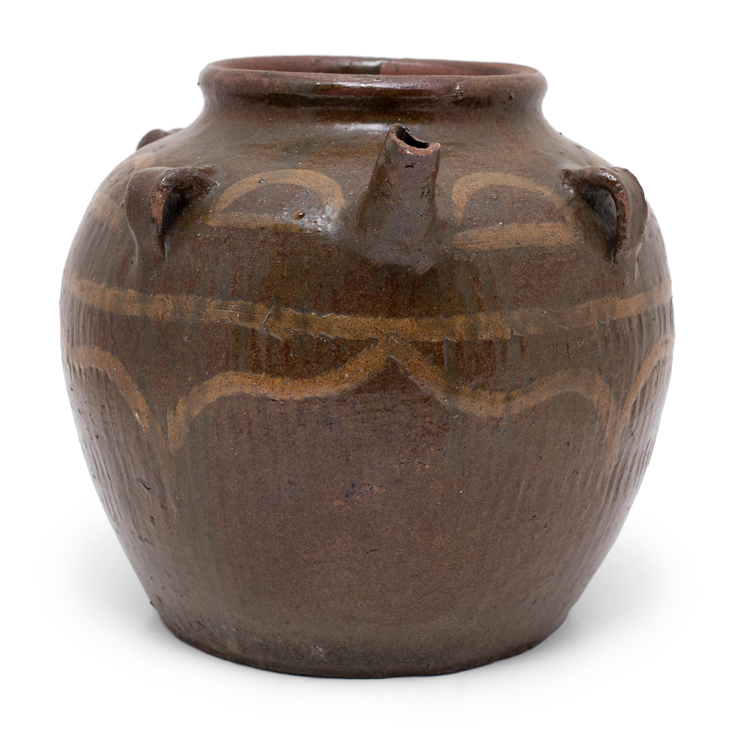 This 19th-century kitchen vessel is coated inside and out with a dark brown glaze that clings to its ribbed sides with subtle color variation. Designed for serving water or tea, the squat jar features a narrow neck, small strap handles, and a short