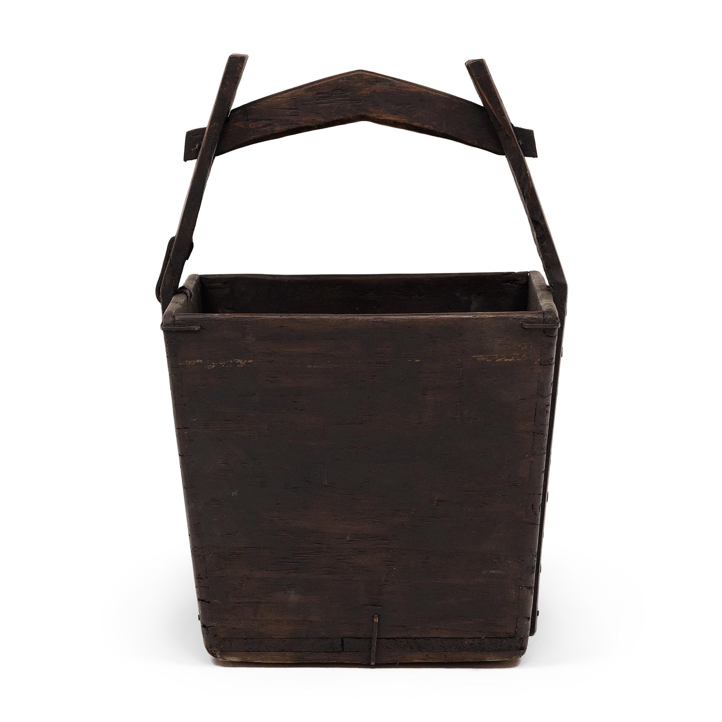 This hand-crafted wooden bucket was once used by farmers in Shanxi, China to transport their harvest of rice and grains over long distances. Counterbalanced by a second container, the pail would have been lifted by a pole threaded through the tall