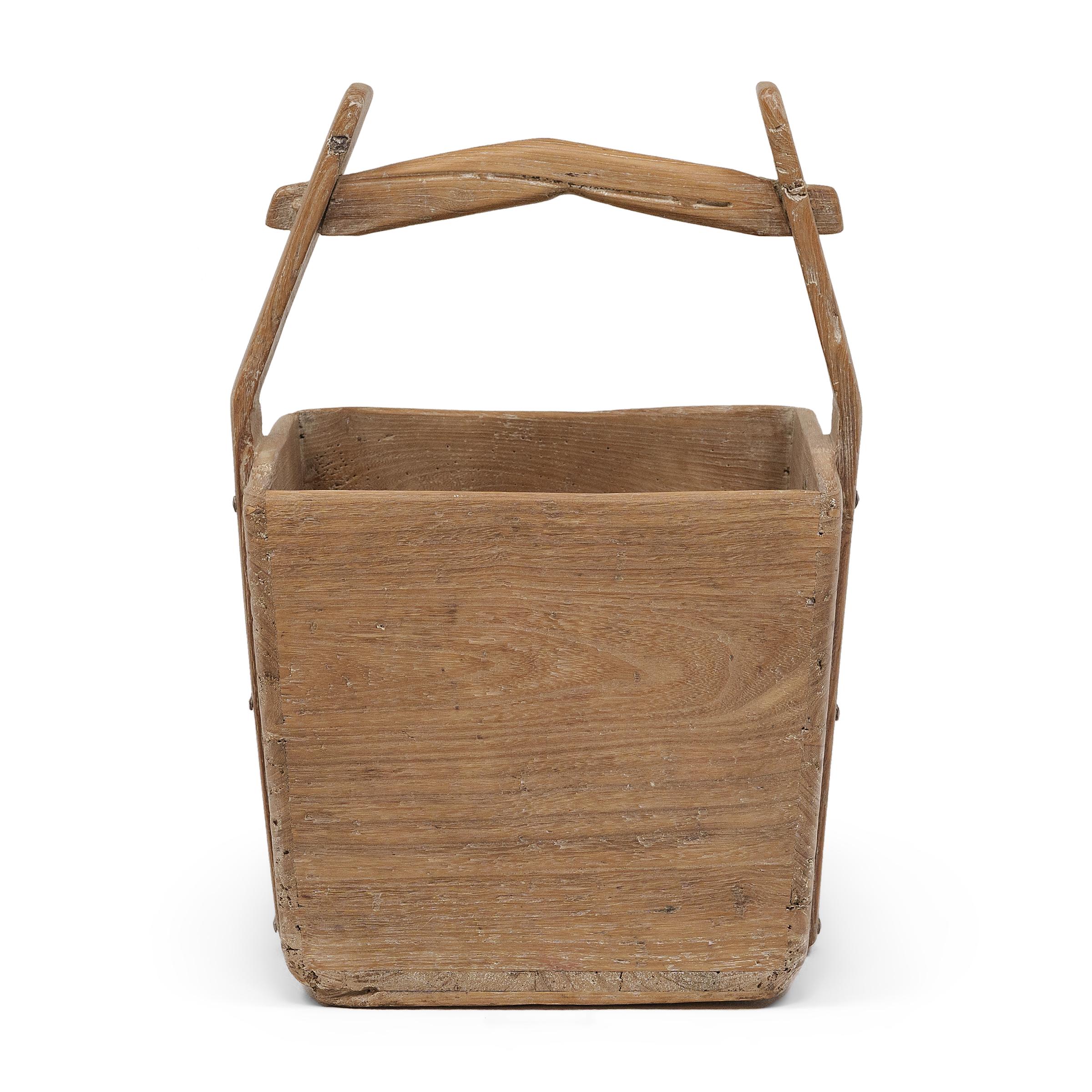 This hand-crafted wooden bucket was once used by farmers in Shanxi, China to transport their harvest of rice and grains over long distances. Counterbalanced by a second container, the pail would have been lifted by a pole threaded through the tall