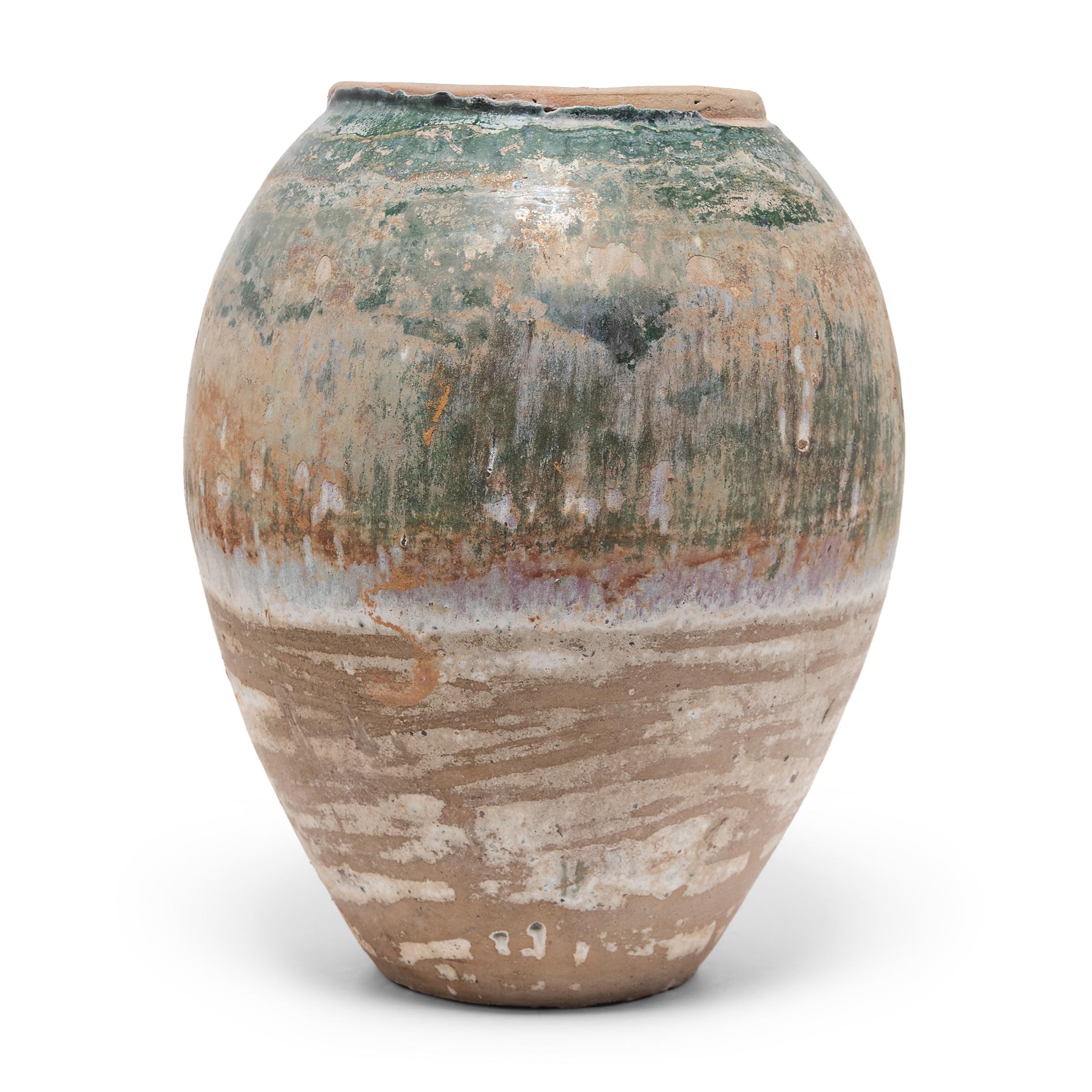 Charged with the humble task of storing dry goods, this large earthenware jar is distinguished by its tapered form and beautifully imperfect glazed exterior. The upper half of the vessel is coated in crackled overglaze that transitions from a glassy