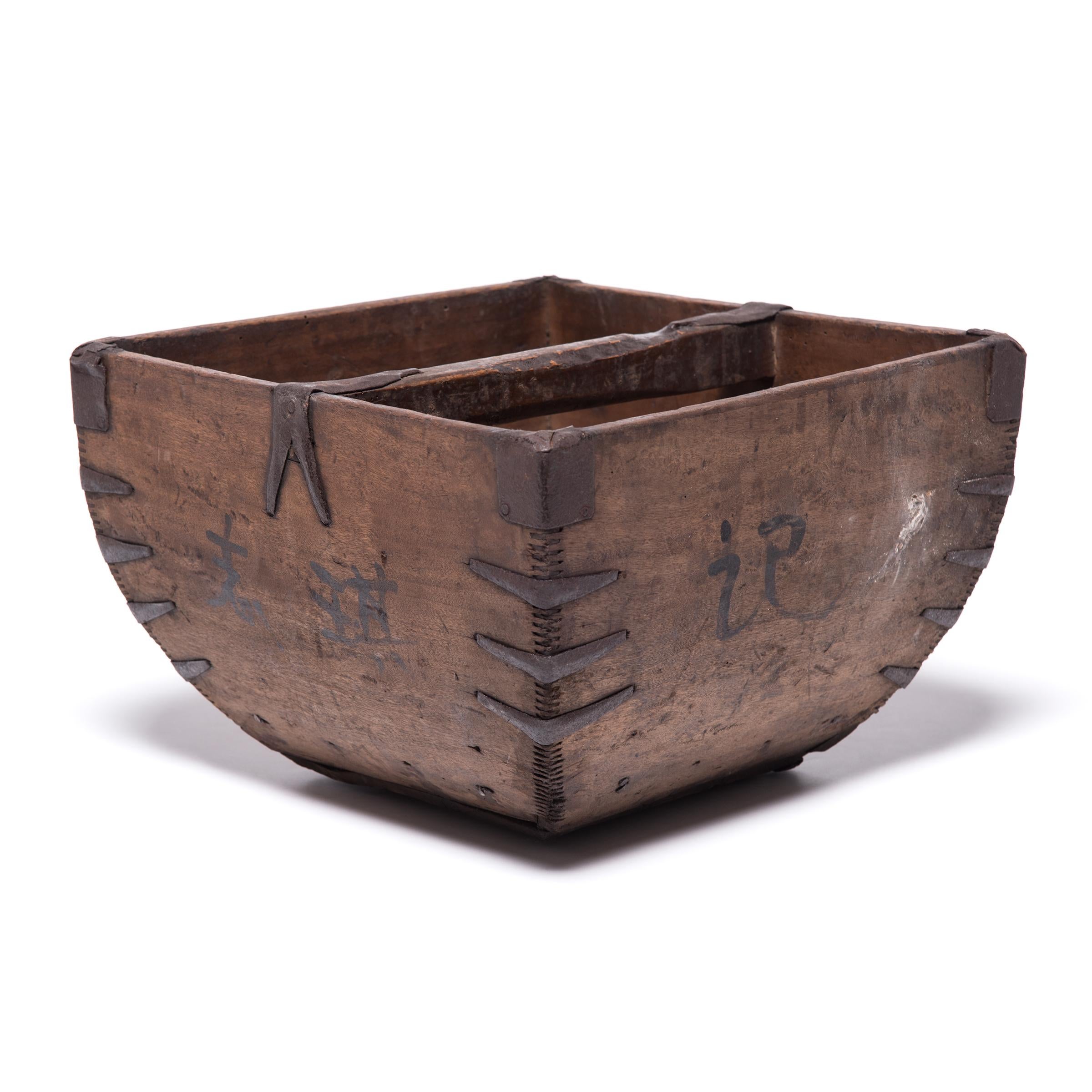 This square container was made over a hundred years ago to measure and hold a dou of rice, an ancient Chinese measurement. It is handcrafted with thin finger joints, iron-finished edges, and a gently arched handle. Marked by painted Chinese