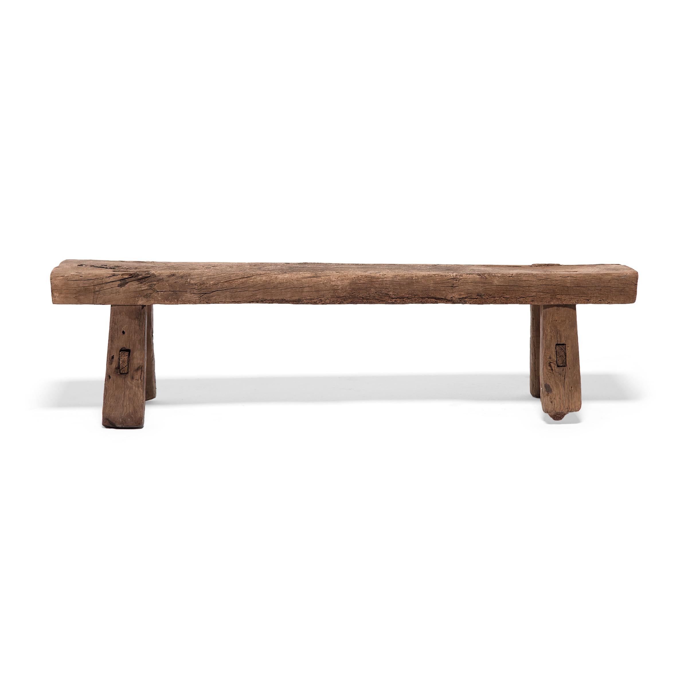 Embracing the raw beauty of unworked wood, this low bench from Hebei province is made from a single piece of unfinished elmwood timber. The plank-top bench was crafted at the turn of the century using mortise-and-tenon joinery techniques, and