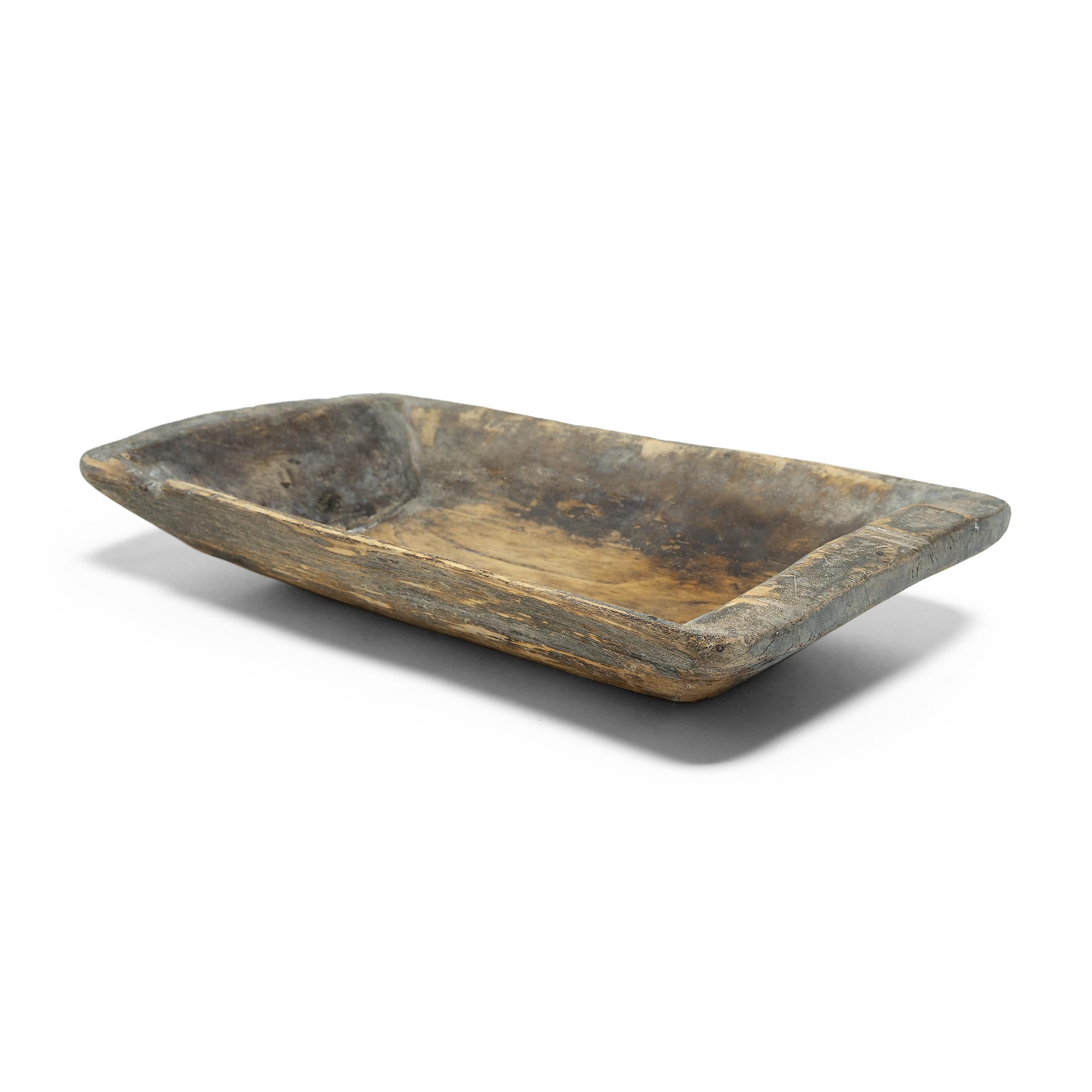 This wooden farm tray from northern China charms with its rustic finish and asymmetrical form. Hand-carved from a single block of wood, the large tray is truly one-of-a-kind, shaped with tapered sides and a shallow interior basin. Years of use have