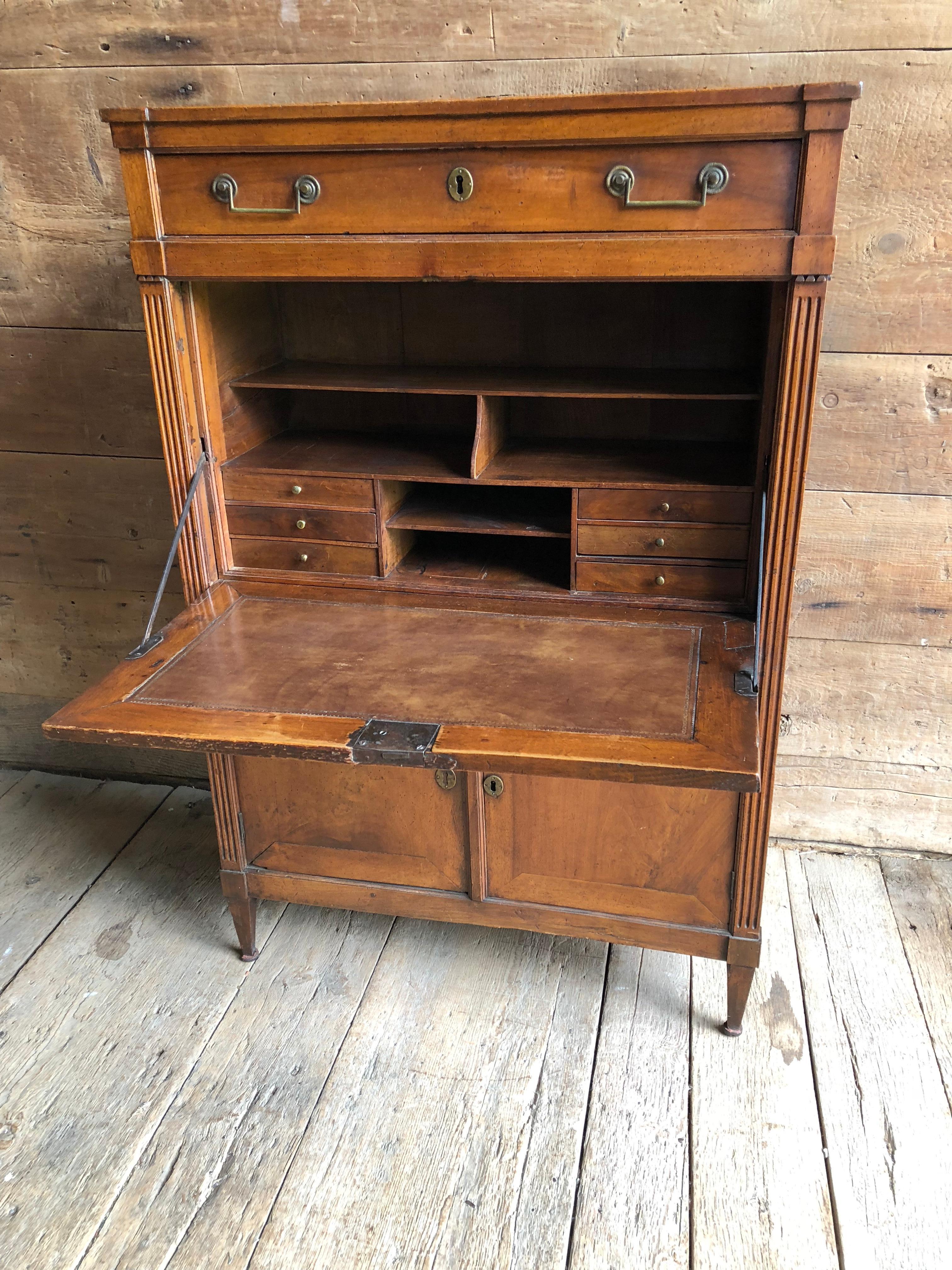 A Provincial fall-front secretaire desk in walnut with original leather writing surface, French Louis XVI, circa 1790. An upper full-length drawer over the fall front compartment over a 2-door lower compartment with shelf and lock box. Original