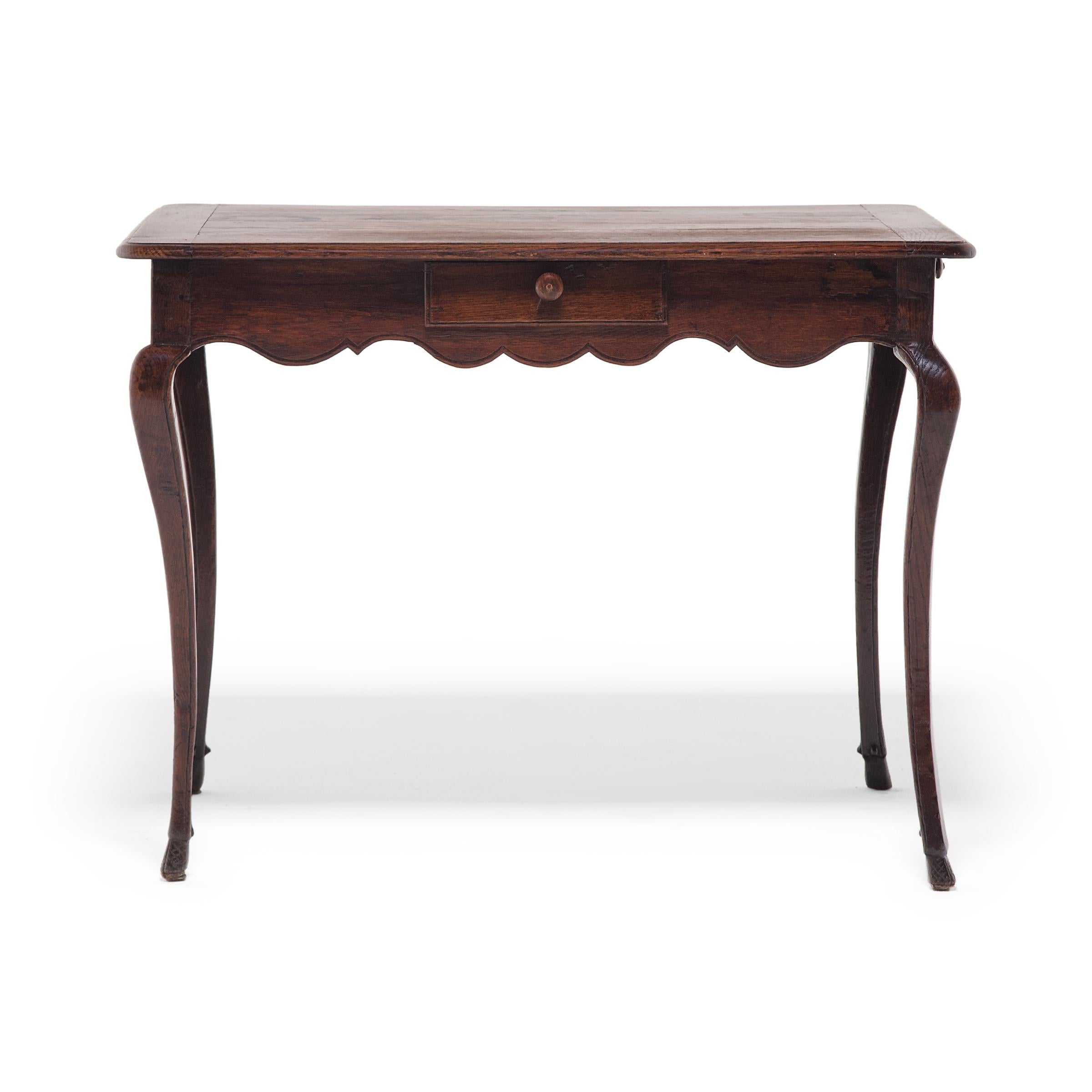 This elegant tea table was crafted of in late-19th-century France in the Louis XV-style, defined by its scalloped apron and thin cabriole legs. The s-form legs curve outwards from the top with dramatic flare, then taper gently to narrow hoof feet