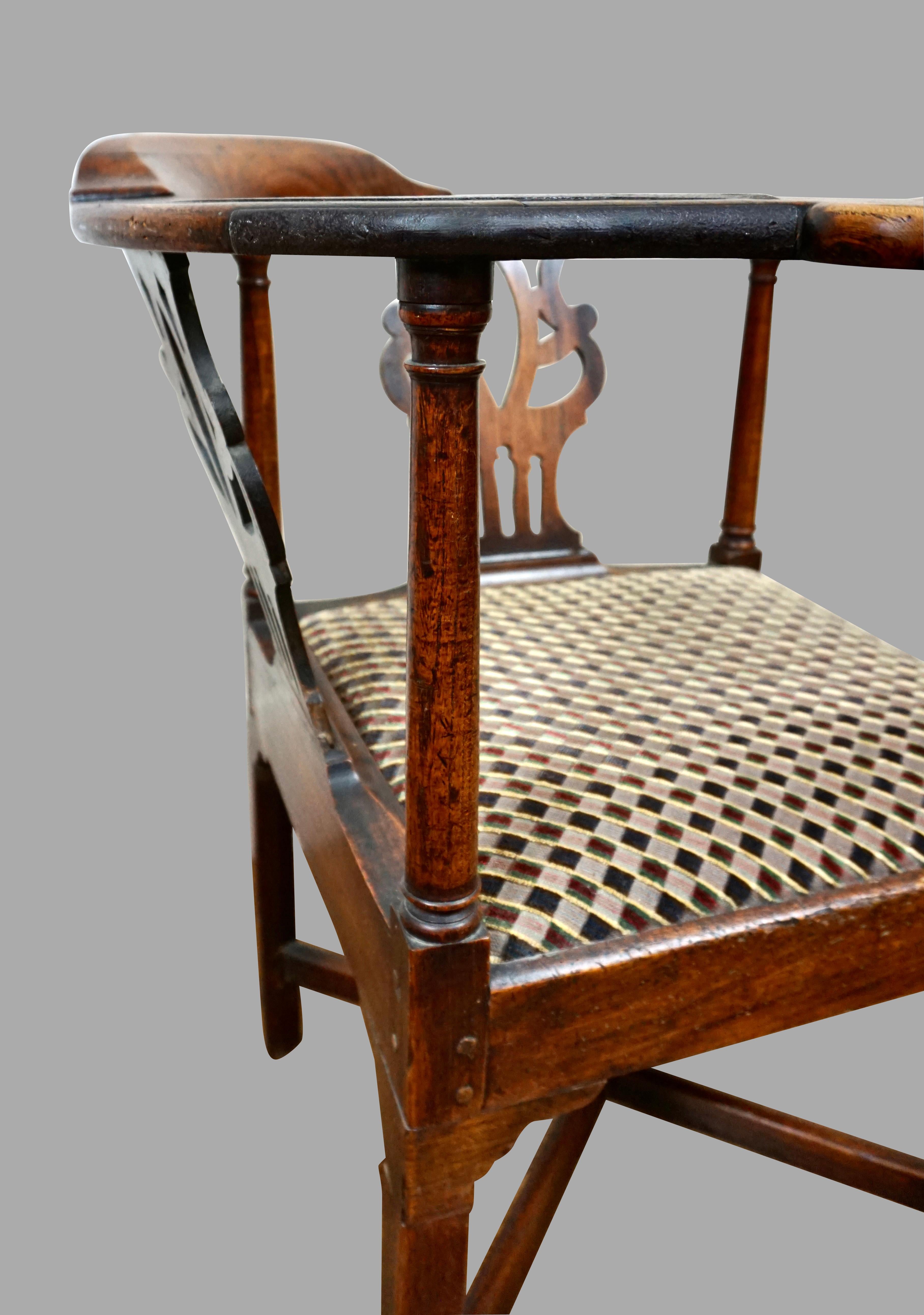 An English Georgian period oak provincial style corner chair of typical form, each side with a pierced splat below the curved chair rail, the drop in seat resting above an X stretcher joining square legs. Circa 1790 or earlier. One arm with a very