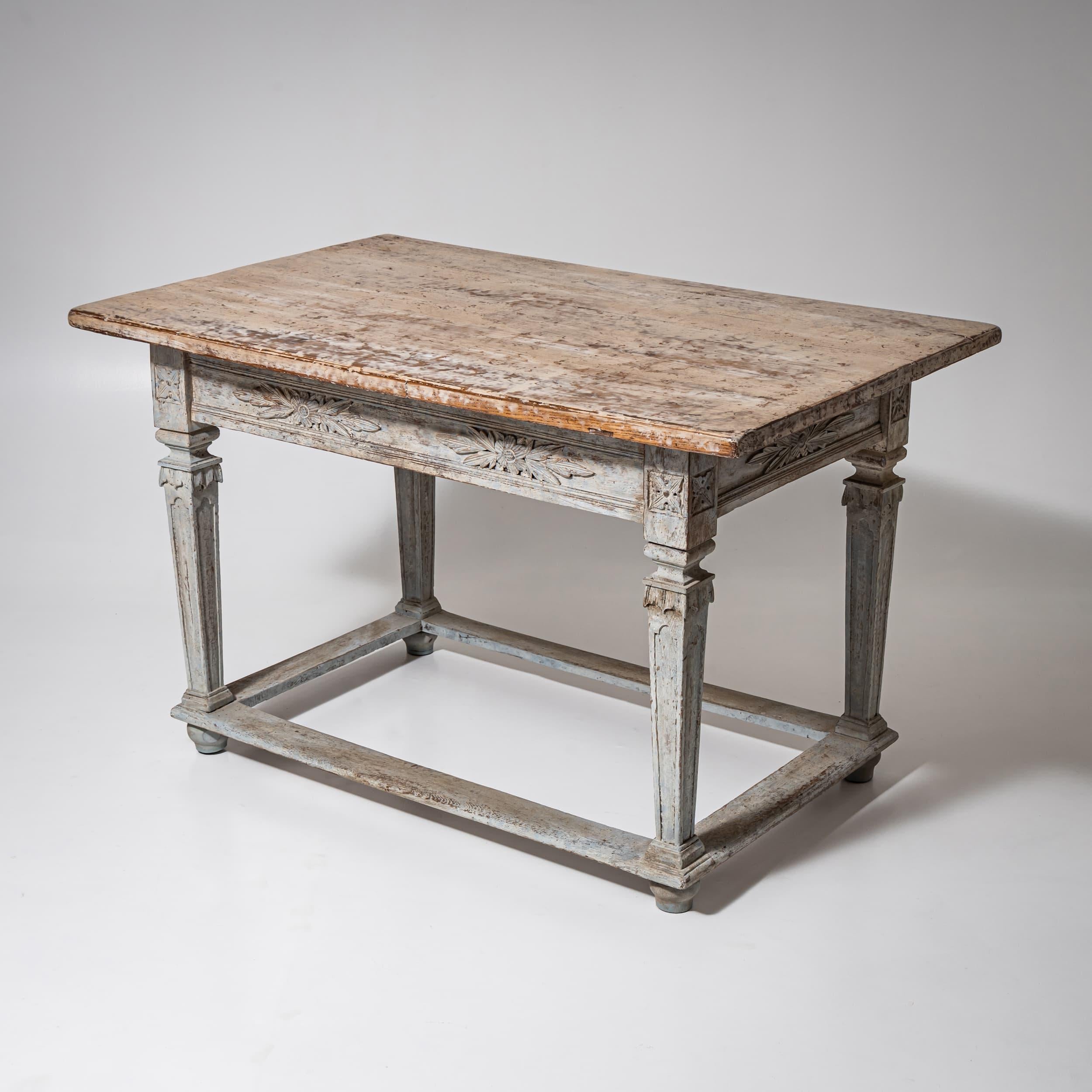 Rechteckiger Louis XVI-Esstisch mit tiefer Schürze, die mit geschnitzten Rosetten und stilisierten Blattmotiven verziert ist. Die gedrechselten Beine sind in typischer Louis Seize-Manier gestaltet und enden in gesockelten Kugelfüßen. Zwischen den