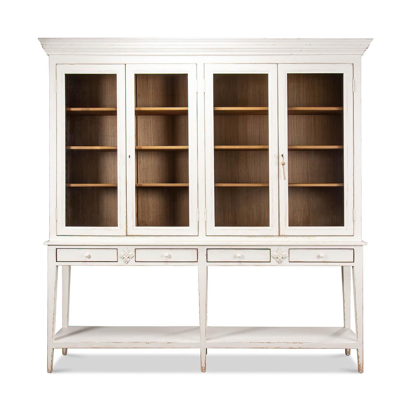 A French provincial-style pine painted display cabinet. The white display case has remarkably subtle details such as slightly splayed legs that are tapered and encase the bottom shelf. Crown molding, with glass front doors that expose a contrasting