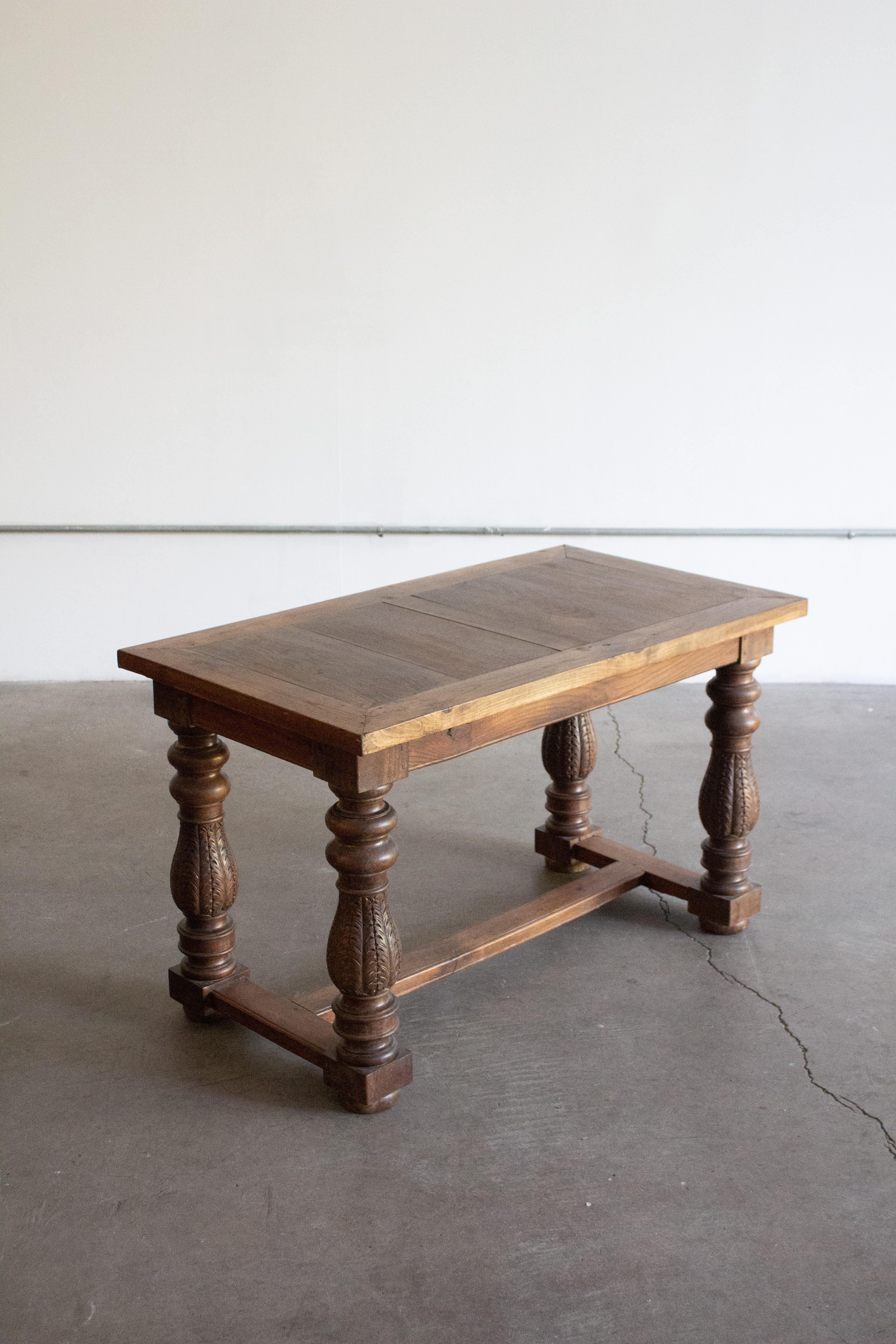 Antiker Tisch aus massivem Hartholz mit einer rechteckigen Bohlenplatte und sichtbaren Tischlerarbeiten. Der Sockel besteht aus vier gedrechselten und geschnitzten Balusterbeinen mit akanthusartigen Motiven, die durch Kastenträger verbunden sind.