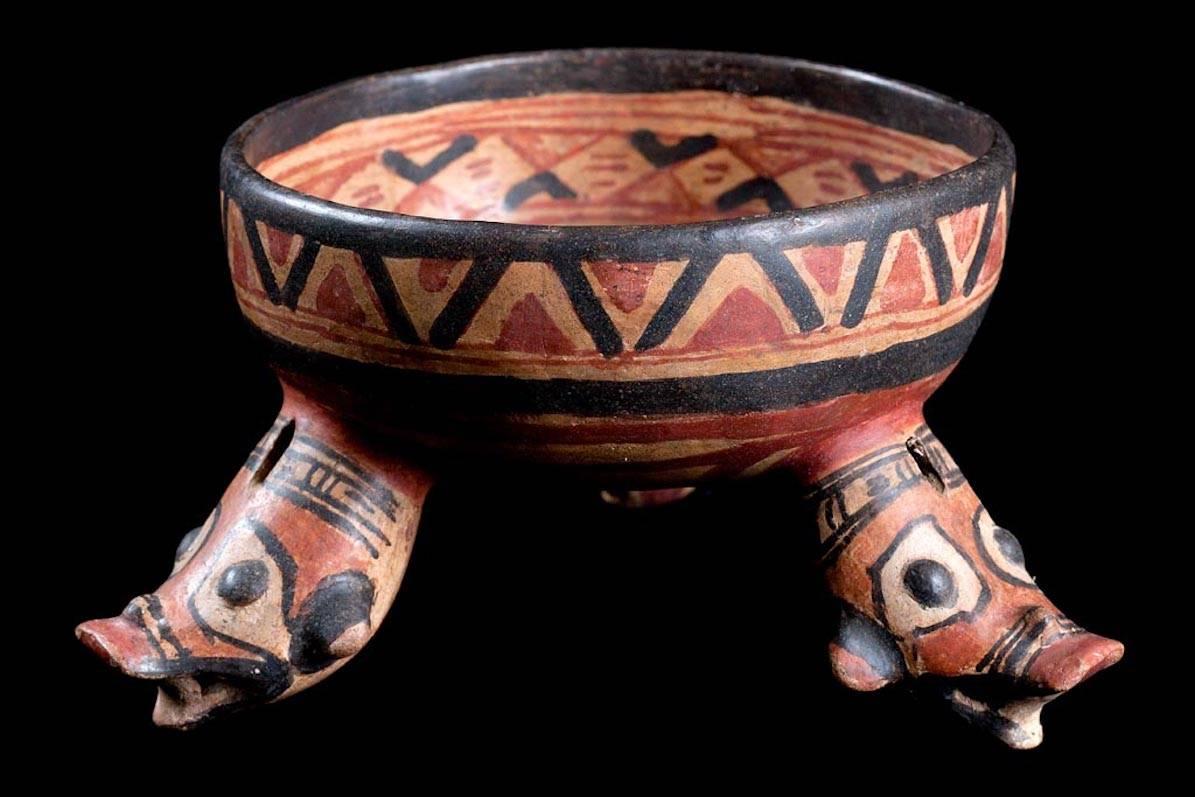 Birmania polychrome pottery tripod bowl having hollow rattle, zoomorphic head type feet. Interior painted decoration probably depicts a stylized alligator motif. Exterior and interior painted bands of geometric decoration. Repaired from