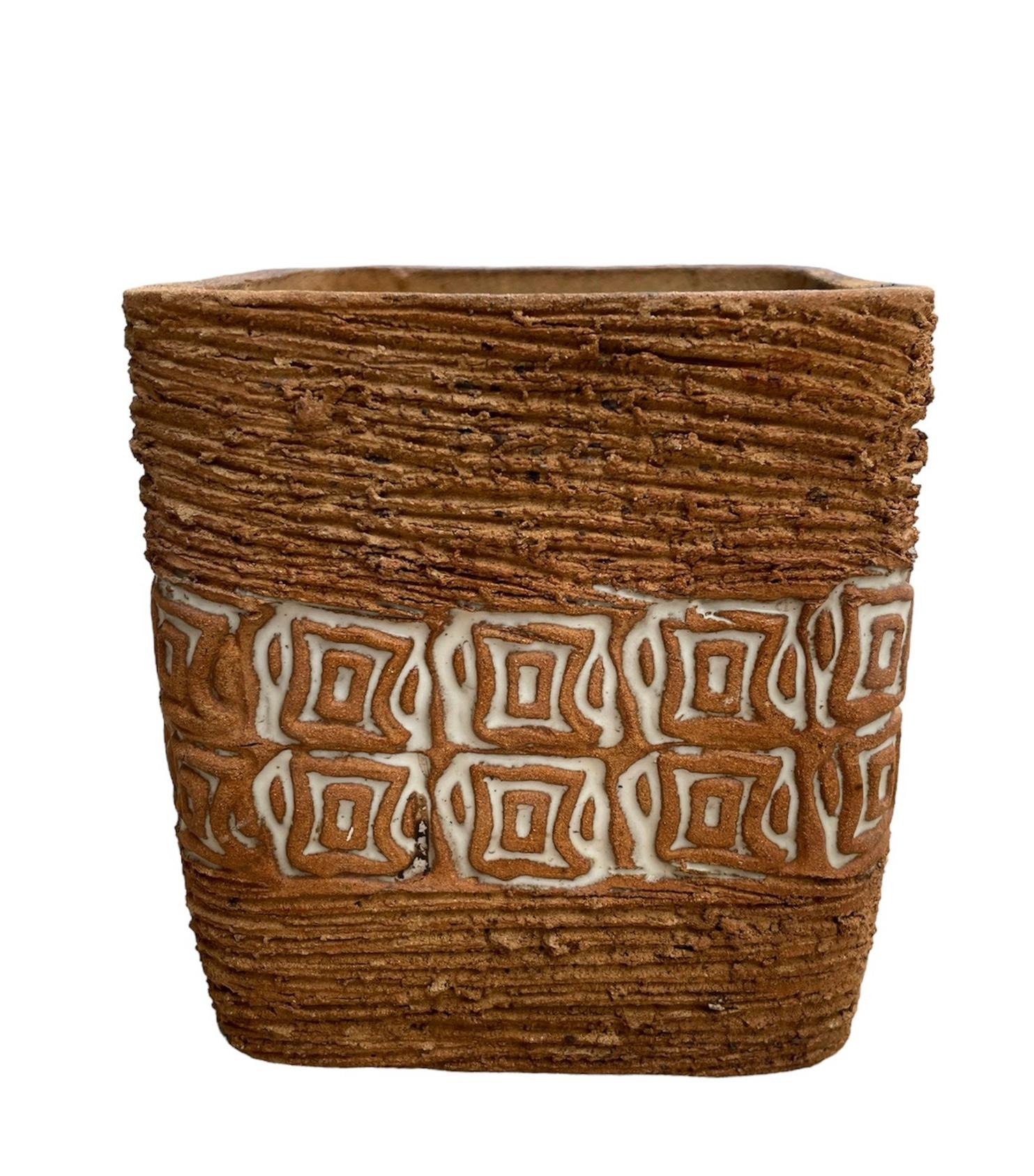 This is a Puerto Rican Stoneware Planter. It depicts a light brown small square planter decorated with a cluster of noodles all around, then its center is enhanced by two rows of small and large squares figures with a white square background. Below