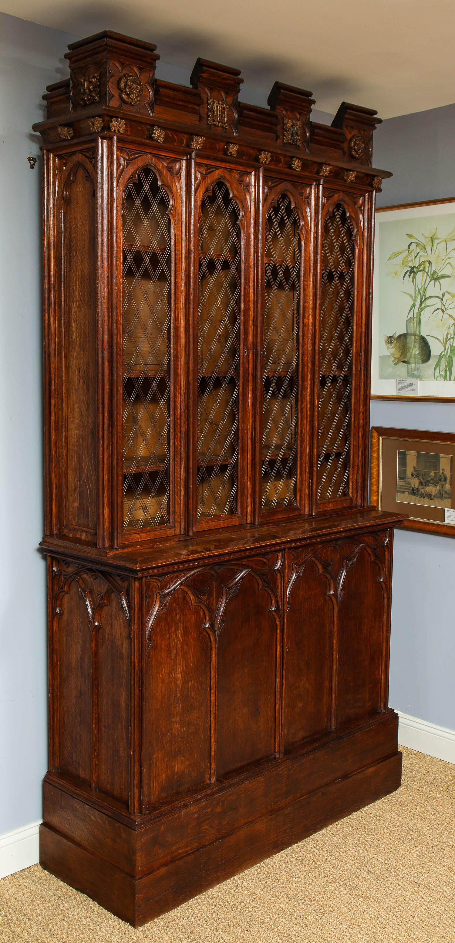 An early 19th century Gothic oak bookcase, the rectangular crenellated top with octafoil panels filled with carved roses, fleur de lis, and a portcullis on a tudor rose back panel above a cavetto frieze mounted with carved oak leaves above two