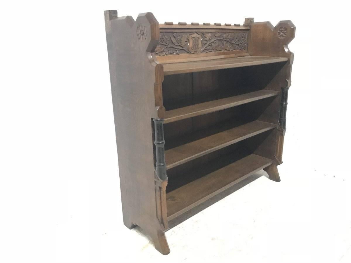 A W N Pugin in the style of, a substantial Gothic Revival open oak bookcase with carved florets, acorns, and oak leaf decoration to the castellated top, centered with a carved shield. The front with turned and part ebonized uprights with wide