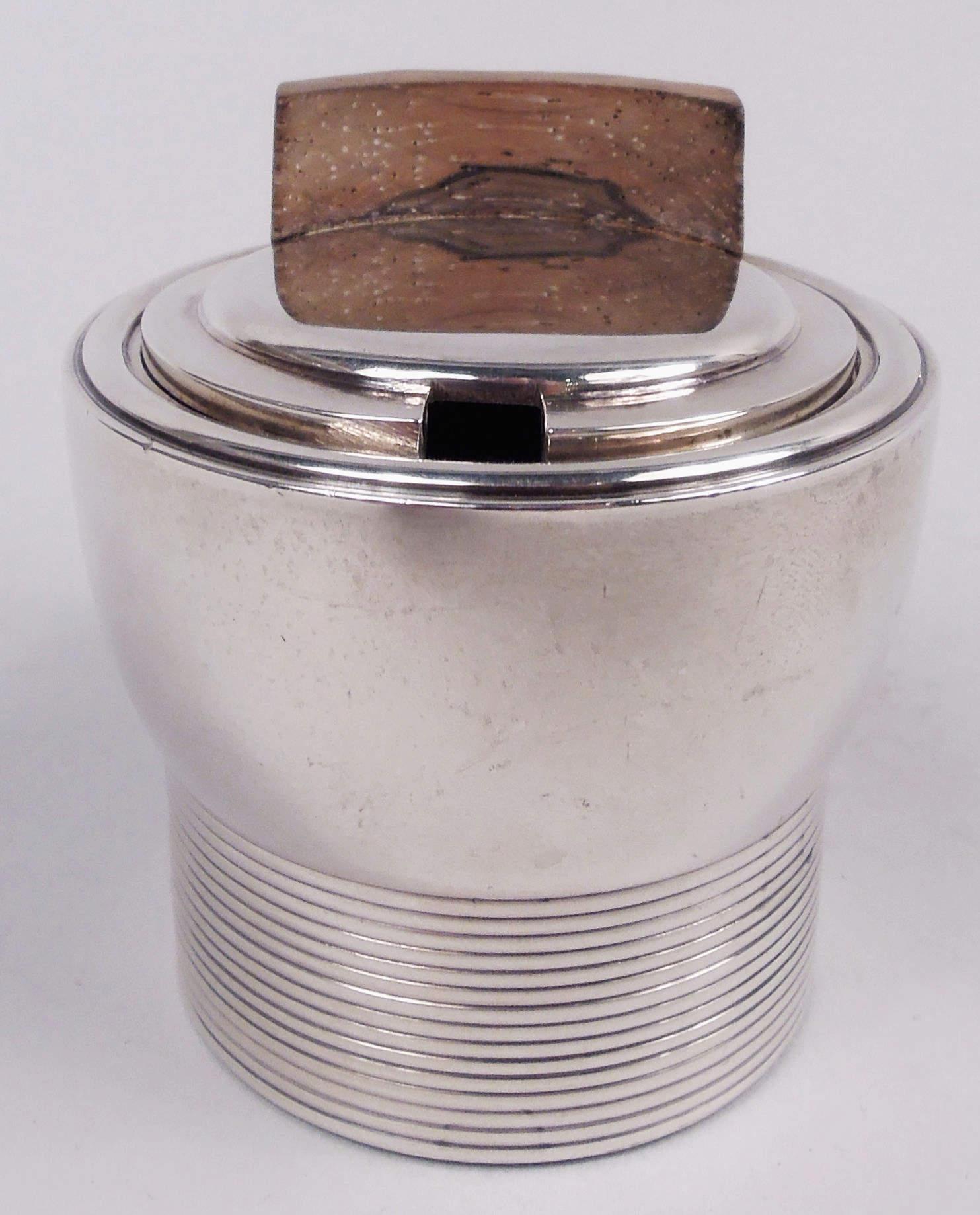 Tarro de mostaza Art Decó de plata 950, hacia 1930. Cazoleta curvada con fondo recto y lengüeta; tapa abatible y escalonada. Monturas de madera teñida: Apoyo facetado para el pulgar y empuñadura abierta en forma de P. Revestimiento de cristal
