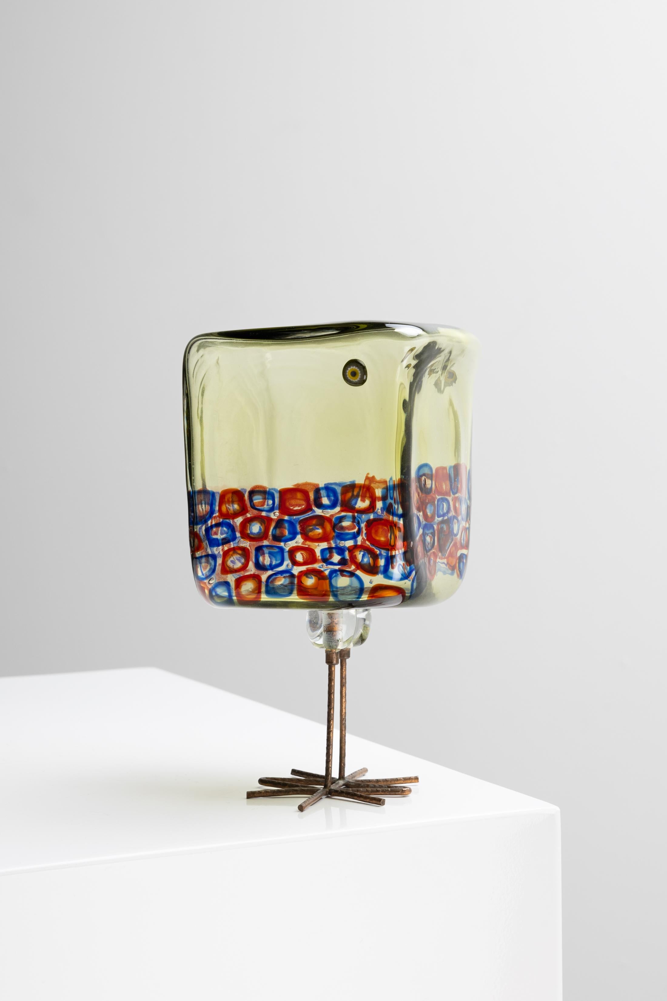 Scultura di un uccello in vetro soffiato con decorazione a murrine, appoggiata su gambe in rame martellato. Disegnato nel 1962 da Alessandro Pianon per Vistosi, Murano (Italia).
Questo uccello in vetro verde scuro (kaki) ha un corpo di forma cubica