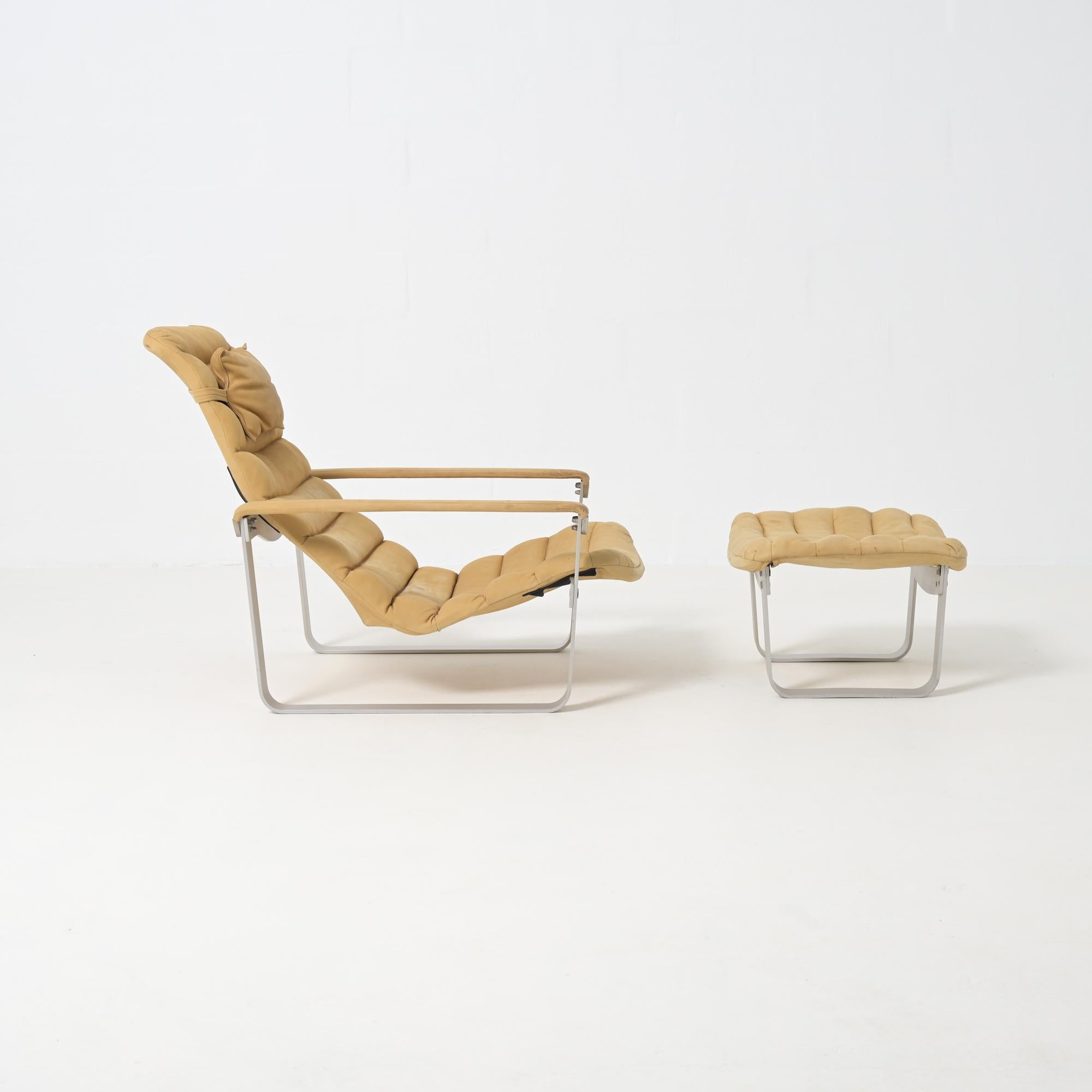 This comfortable minimalist armchair with ottoman was designed by the Finnish designer Ilmari Lappalainen for Asko. The design from 1968 is characterized by its cushion-like seating element in natural nubuck, it hangs in a sturdy aluminum frame. The
