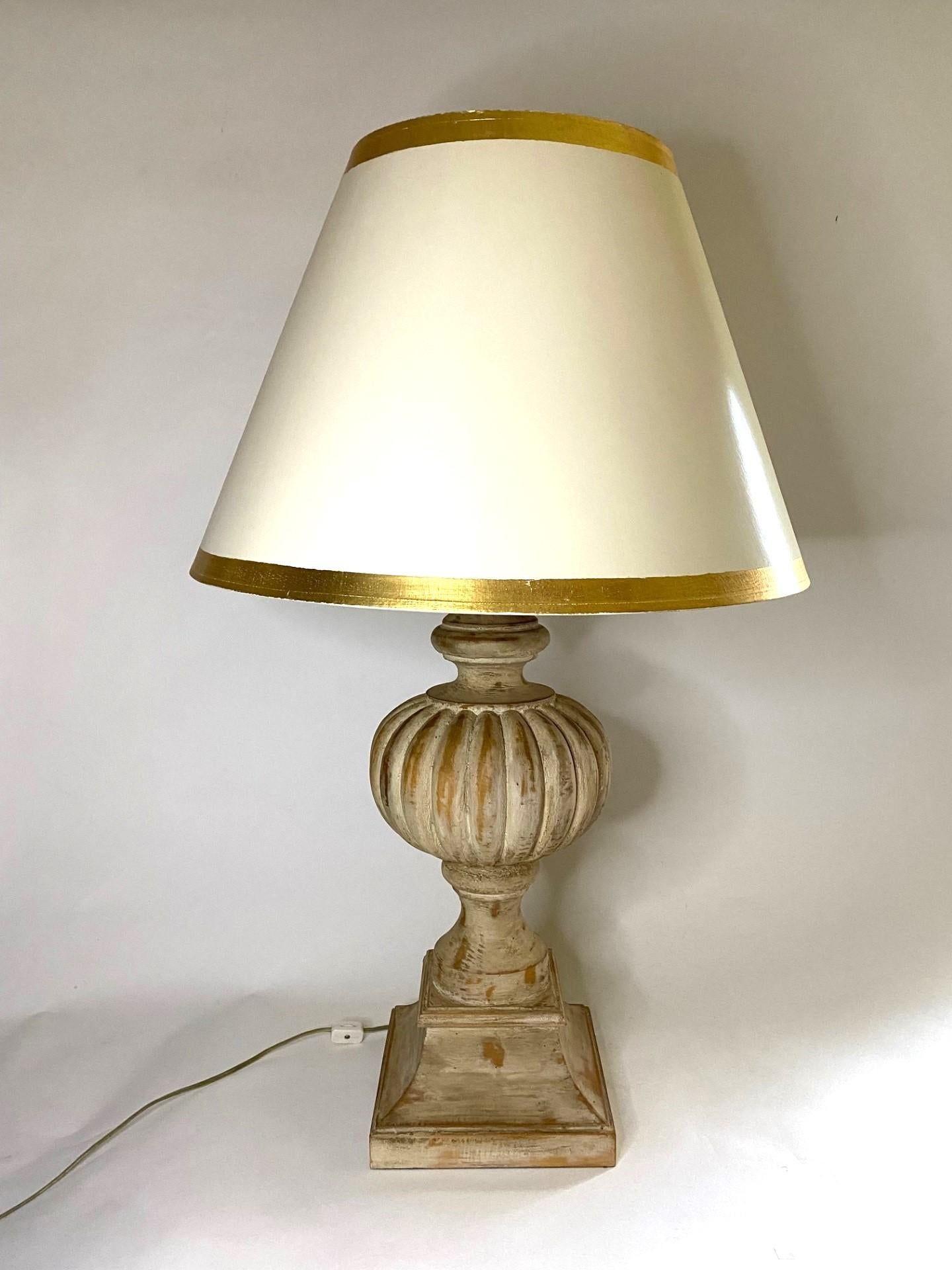 Attrayante lampe de table en bois sculpté, blanc antique et lavé, avec abat-jour tambour blanc et bordure dorée. 