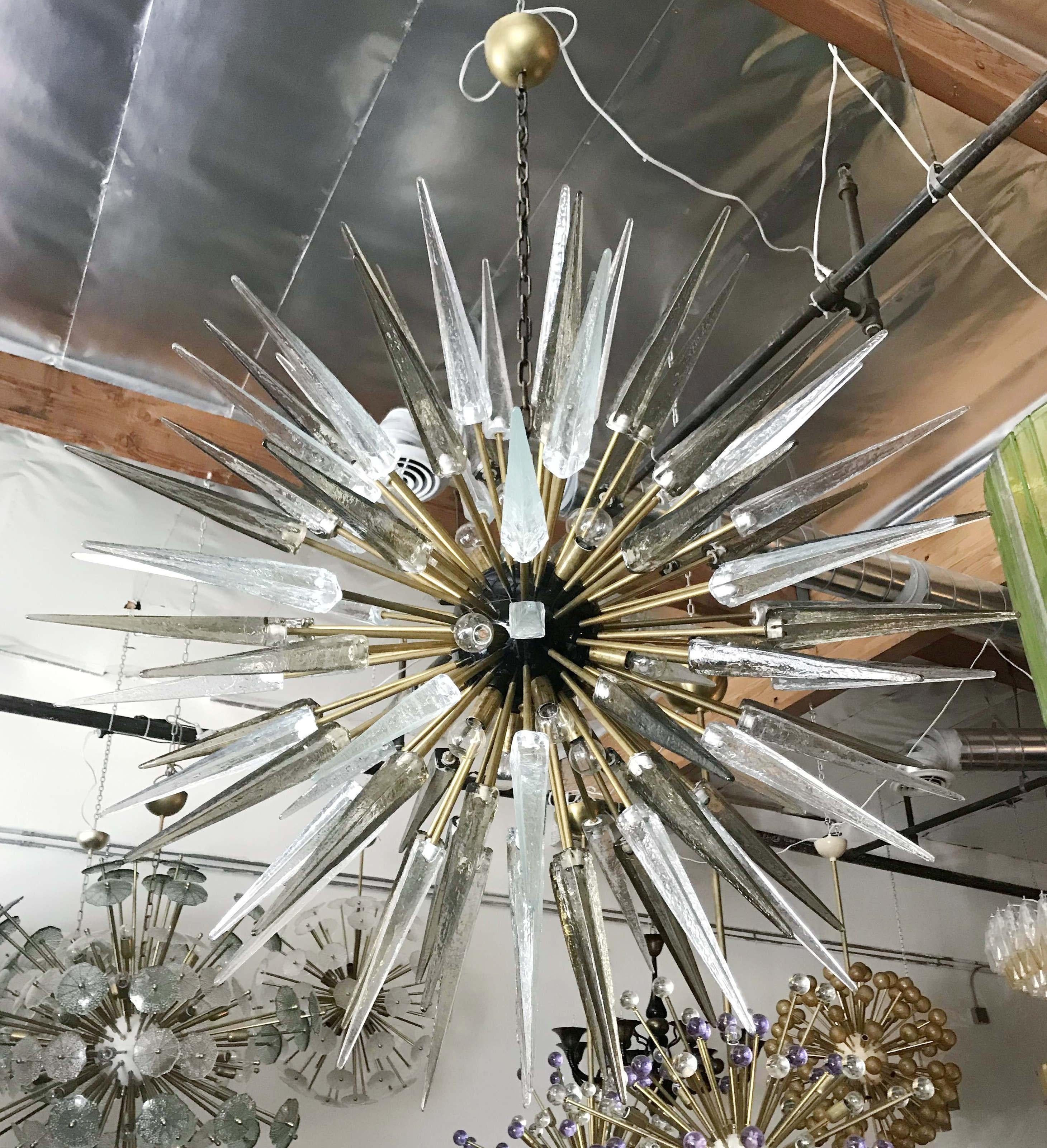 Lampadario italiano moderno a sputnik con punte in vetro di Murano chiaro e fumé, montato su una struttura in ottone naturale non laccato con centro smaltato nero, disegnato da Fabio Bergomi per Fabio Ltd / Made in Italy
16 luci / tipo E12 o E14 /