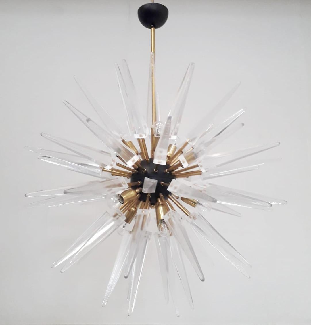 Lampadario sputnik moderno italiano con punte in vetro di Murano trasparente, montato su una struttura in ottone naturale non laccato con centro e baldacchino nero opaco, disegnato da Fabio Bergomi per Fabio Ltd / Made in Italy 
12 luci / tipo E12 o