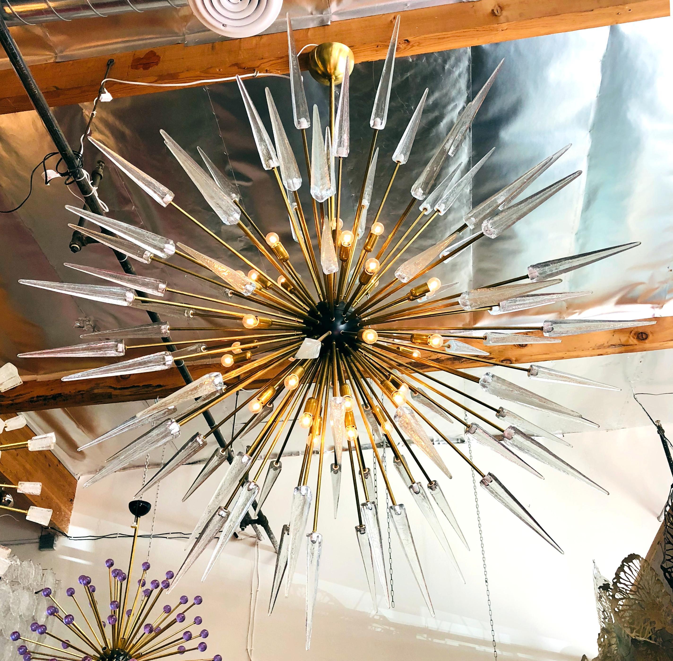 Lampadario sputnik moderno italiano con punte in vetro di Murano trasparente, montato su una struttura in ottone naturale non laccato con centro smaltato nero, disegnato da Fabio Bergomi per Fabio Ltd / Made in Italy
30 luci / tipo E12 o E14 / max