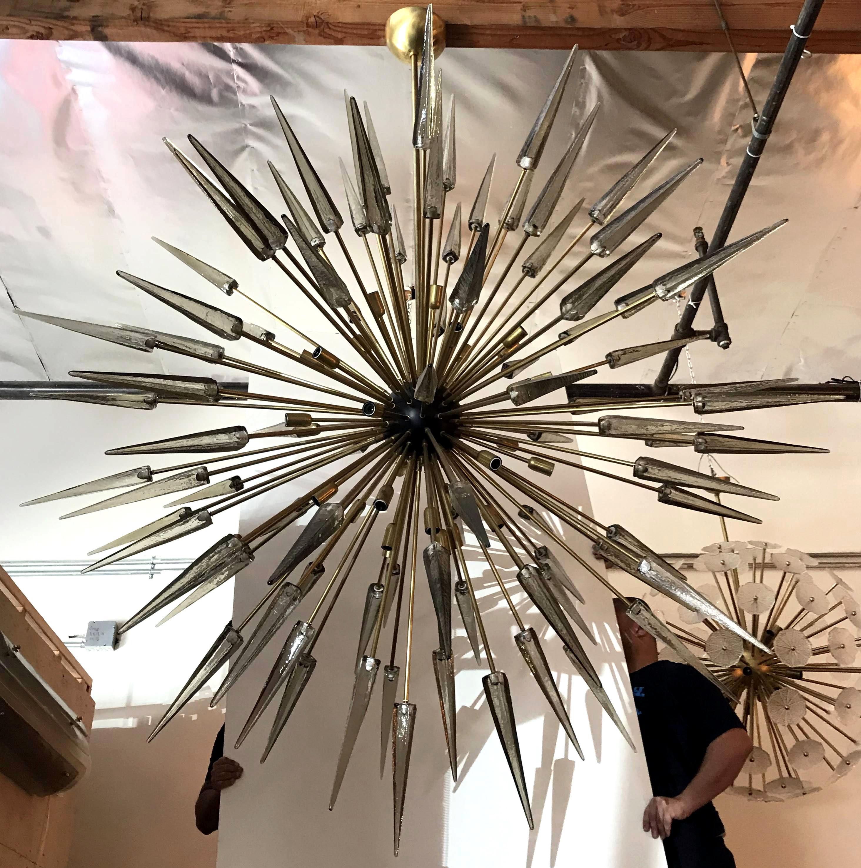 Lampadario sputnik moderno italiano con punte di frammenti di vetro di Murano fumé, montato su una struttura in ottone naturale non laccato con centro smaltato nero, disegnato da Fabio Bergomi per Fabio Ltd / Made in Italy
30 luci / tipo E12 o E14 /