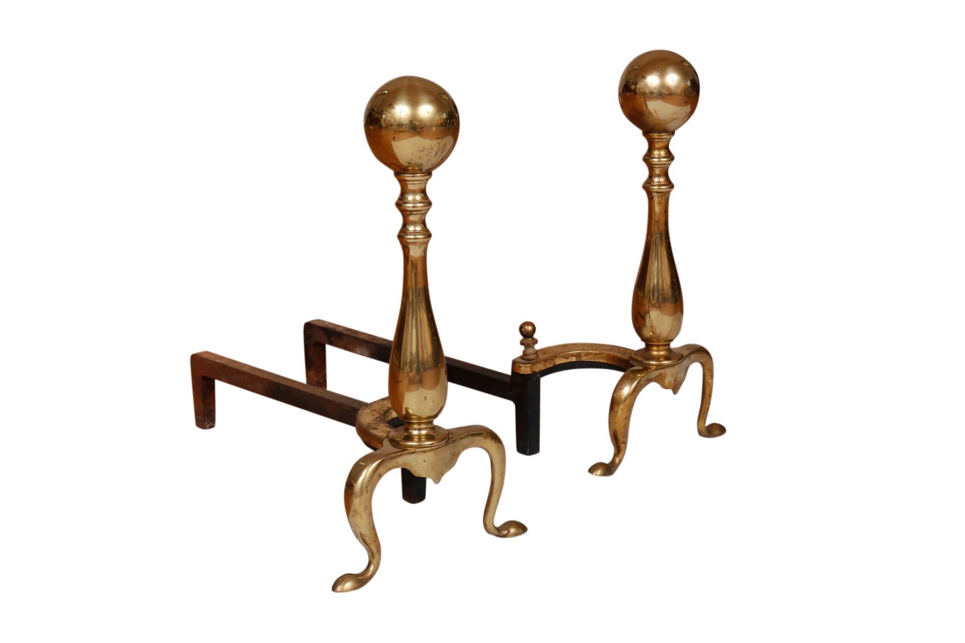 A pair of ball topped brass andirons made by Puritan Manufacturing Co. Elegant turned plinths are supported with serpentine legs finished with snake feet. Iron billet bars are pressed with the makers mark “Puritan”. Dimensions per andiron.
