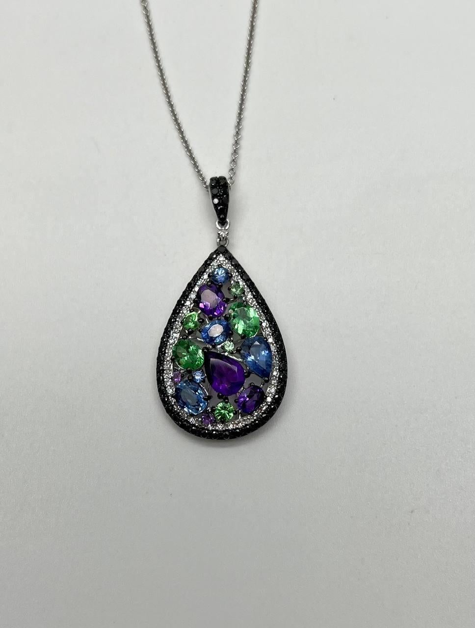 A stunning pendant necklace, this exquisite piece features a teardrop-shaped pendant adorned with an array of vibrant gemstones in purple, green, and blue hues.
The gemstones are set within a dark, elegant frame of black diamonds, bordered by a