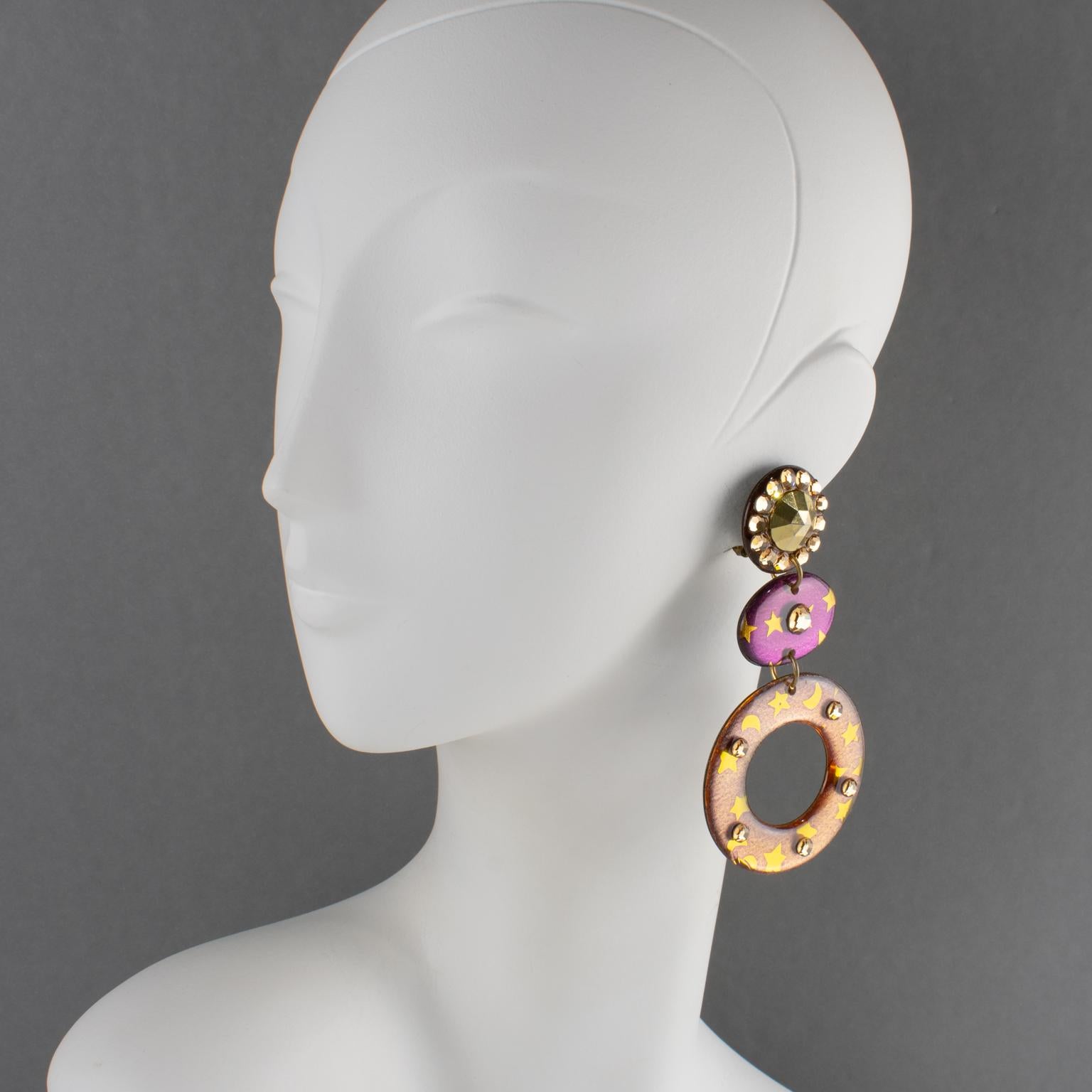 These gorgeous Italian acrylic resin or Lucite dangling clip-on earrings feature an oversized chandelier shape with a large donut design in amethyst purple and antique rose colors adorned with stars and crescents in gold color. The purple and